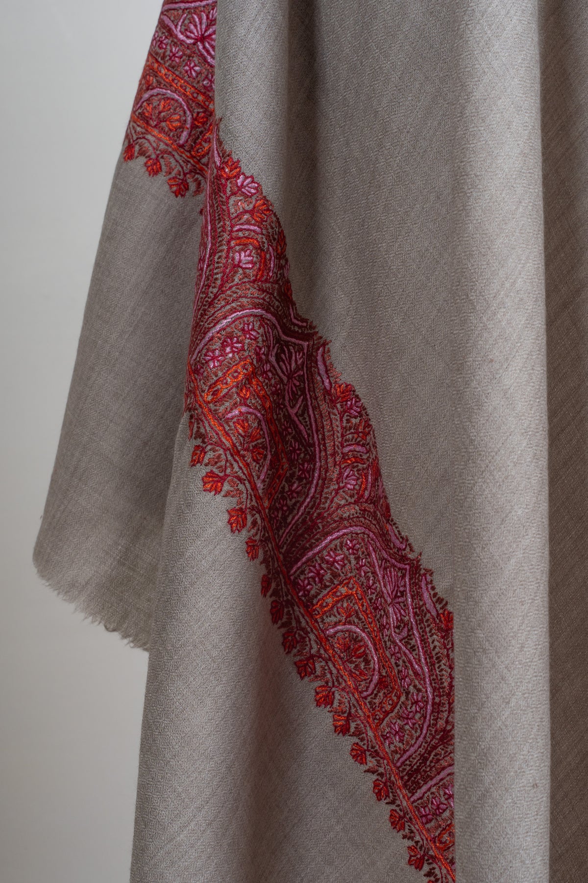 Grey shawl drape showing its crimson and pink patterned border and lightly fringed edge.
