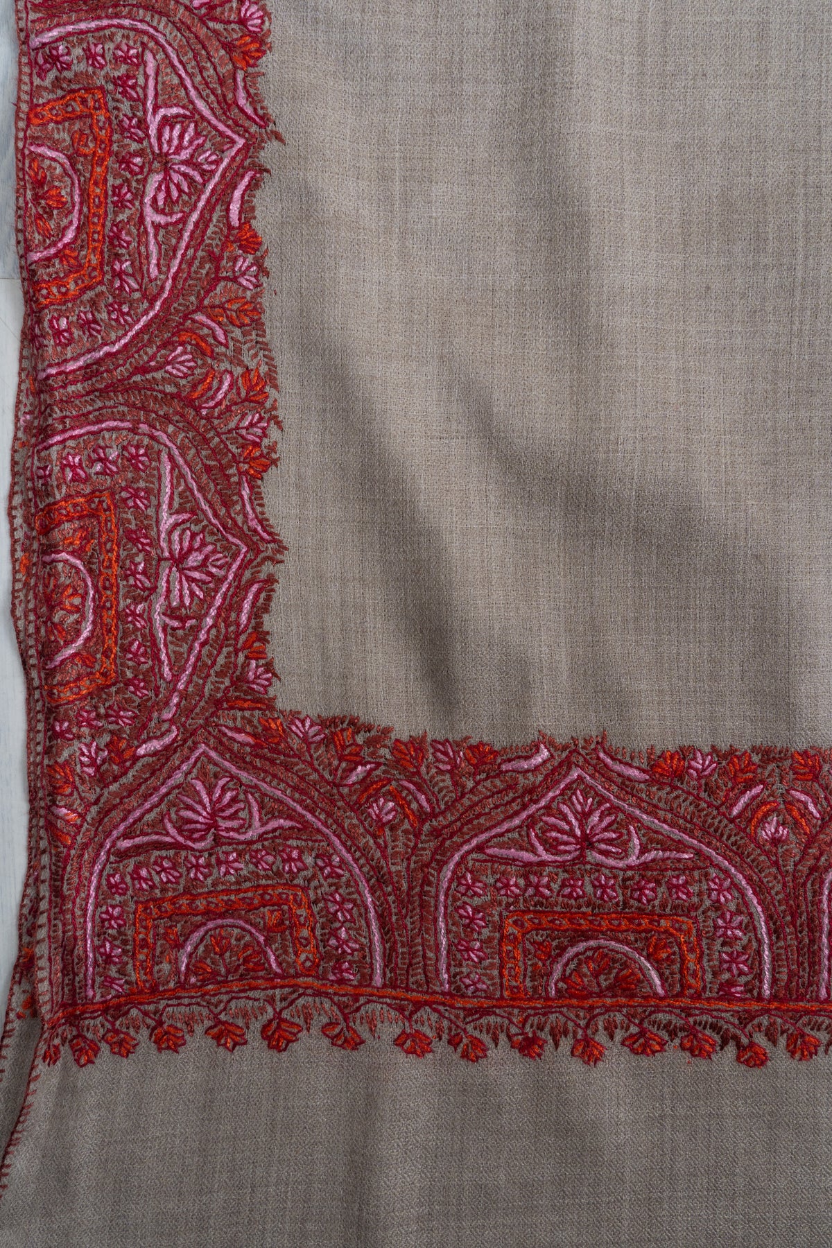 Corner detail of the grey shawl with crimson and pink arch-shaped floral embroidery.