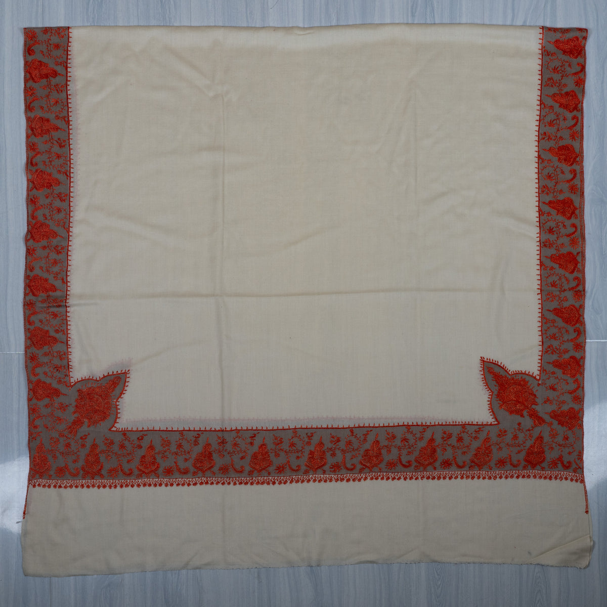 Ivory Merino wool shawl laid flat, with red floral borders, large lower corner motifs and a broad plain end panel