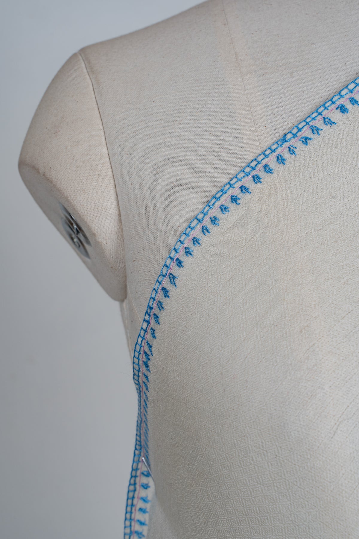 Shoulder close-up of the ivory shawl's narrow blue embroidered edge and small leaf motifs