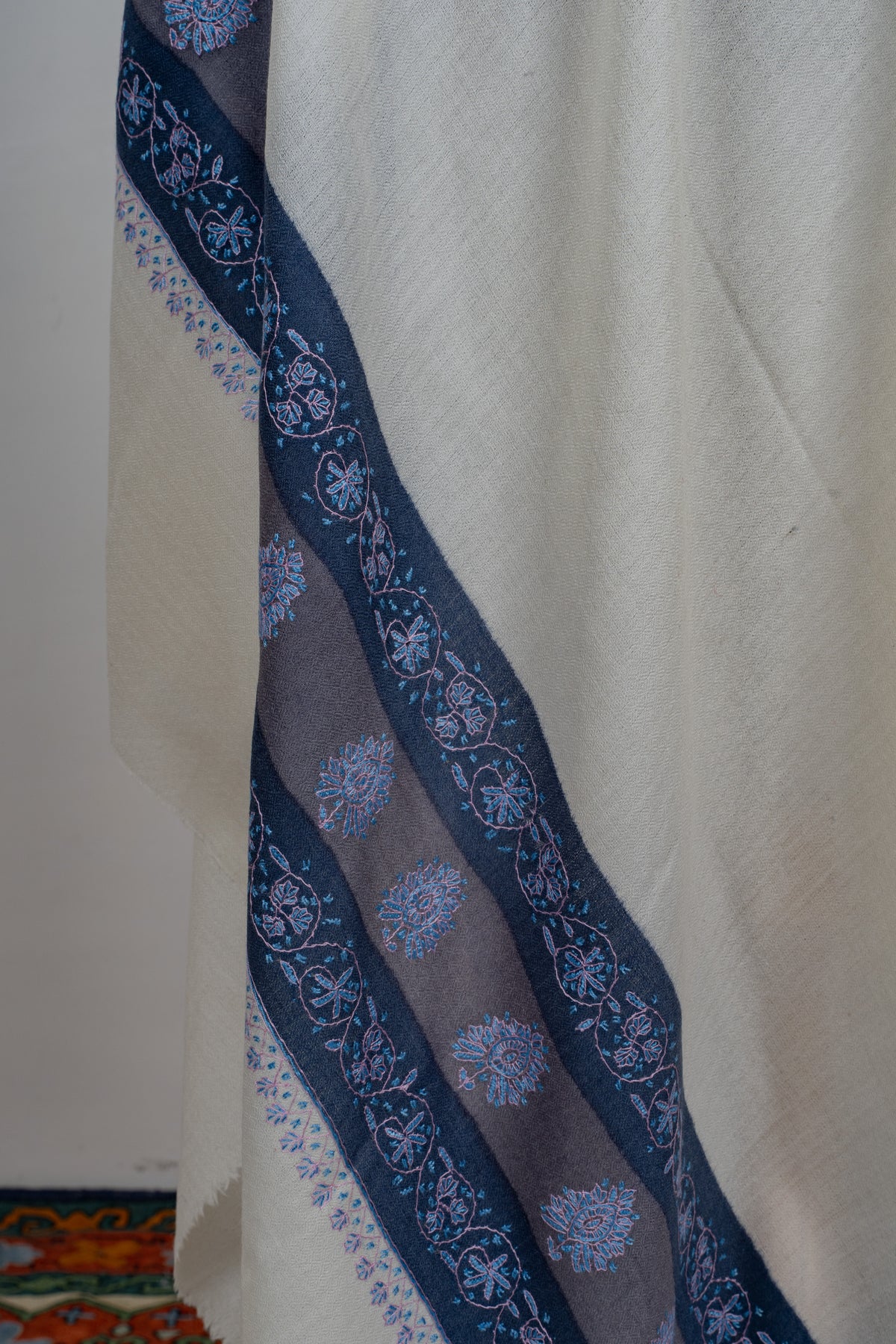 Draped detail of the ivory shawl showing navy and grey-blue bands with pale blue floral embroidery