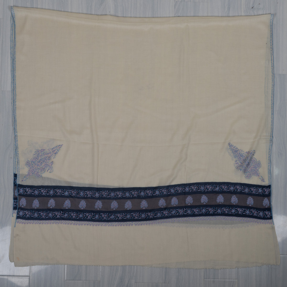 Ivory Merino wool shawl spread flat with navy floral bands, pale blue paisley corner motifs and a plain end