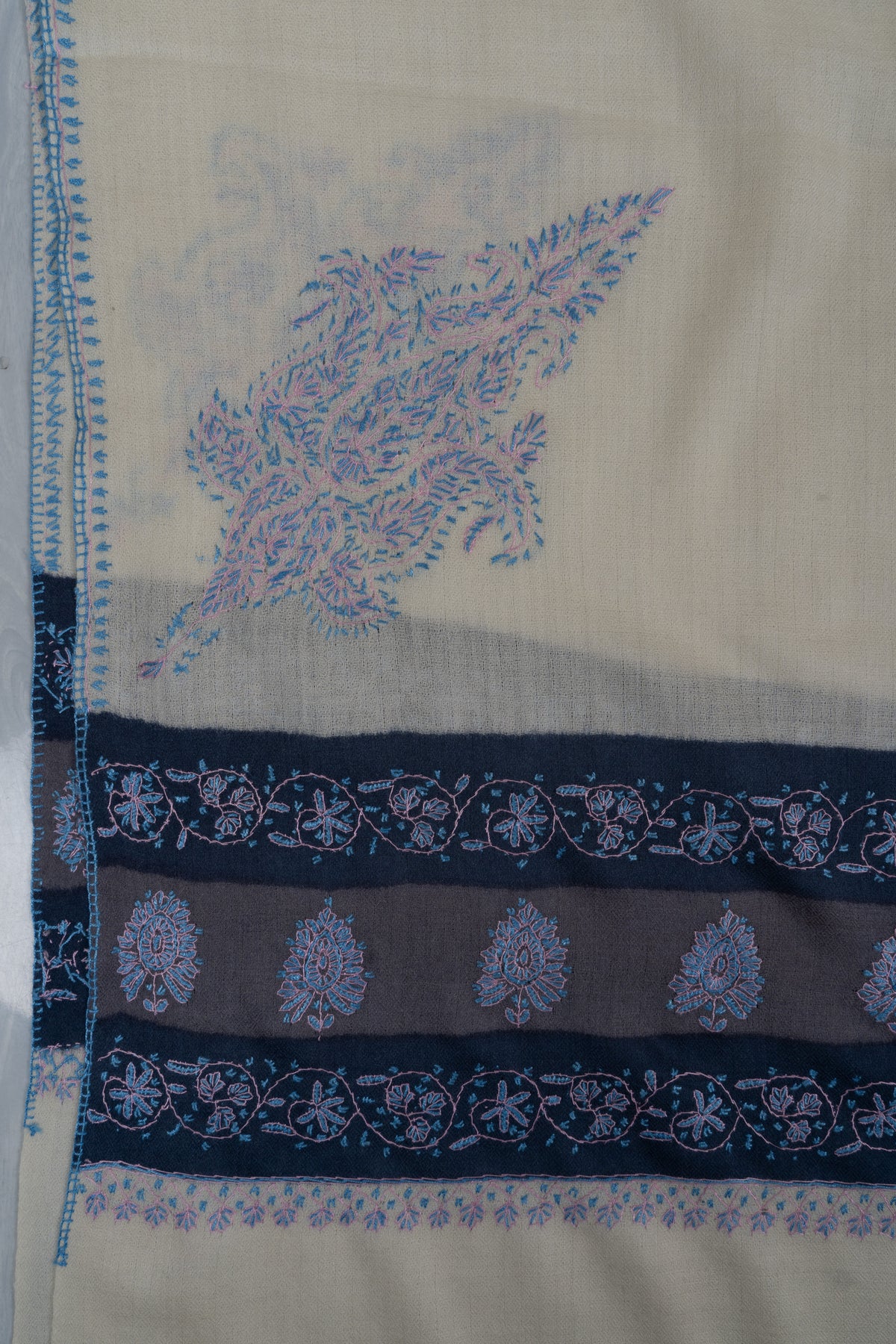 Corner detail of the ivory shawl with a pale blue paisley motif above navy embroidered bands