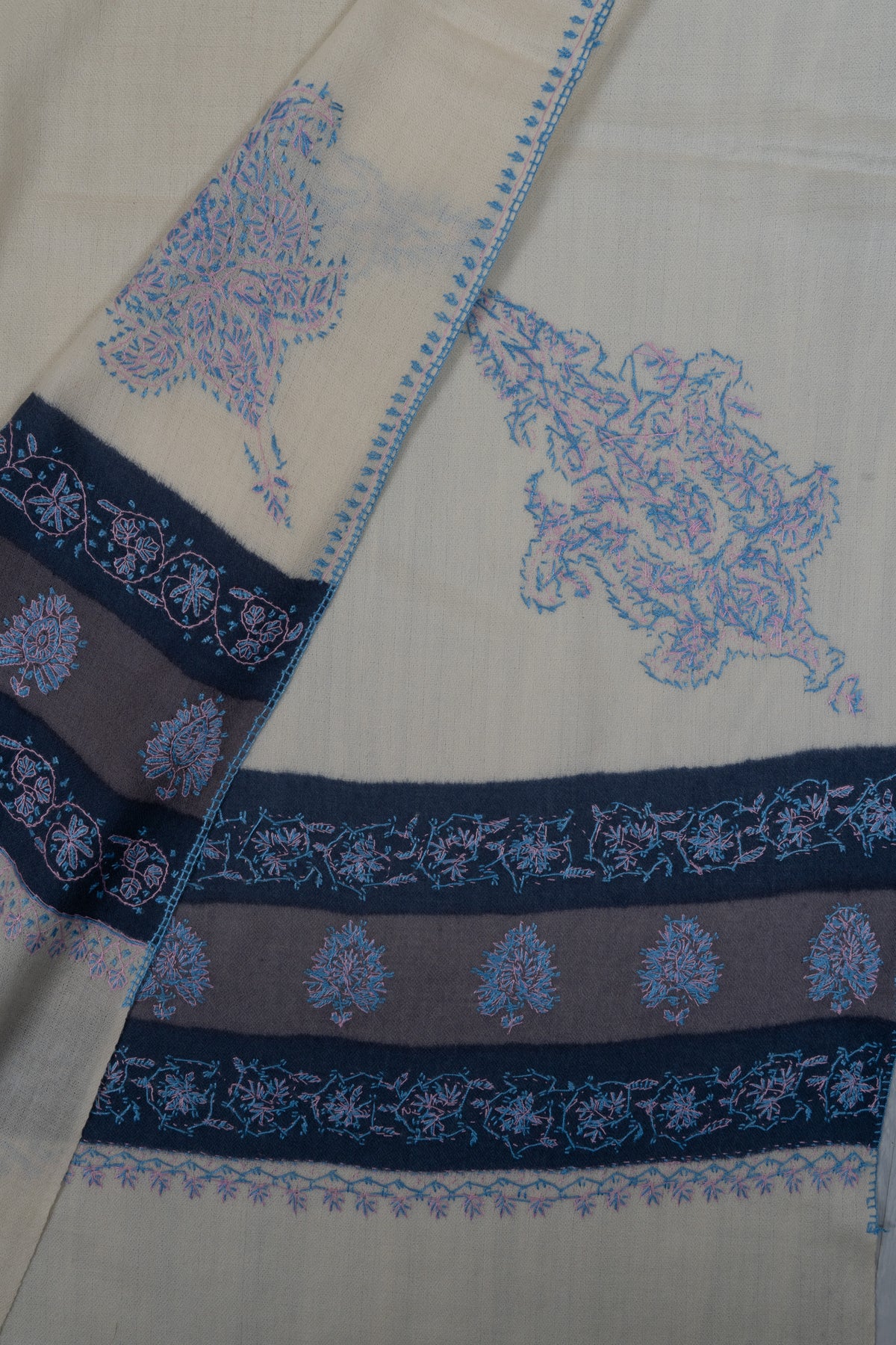 Folded ends of the ivory shawl showing blue Sozni borders and paisley corner motifs on both sides