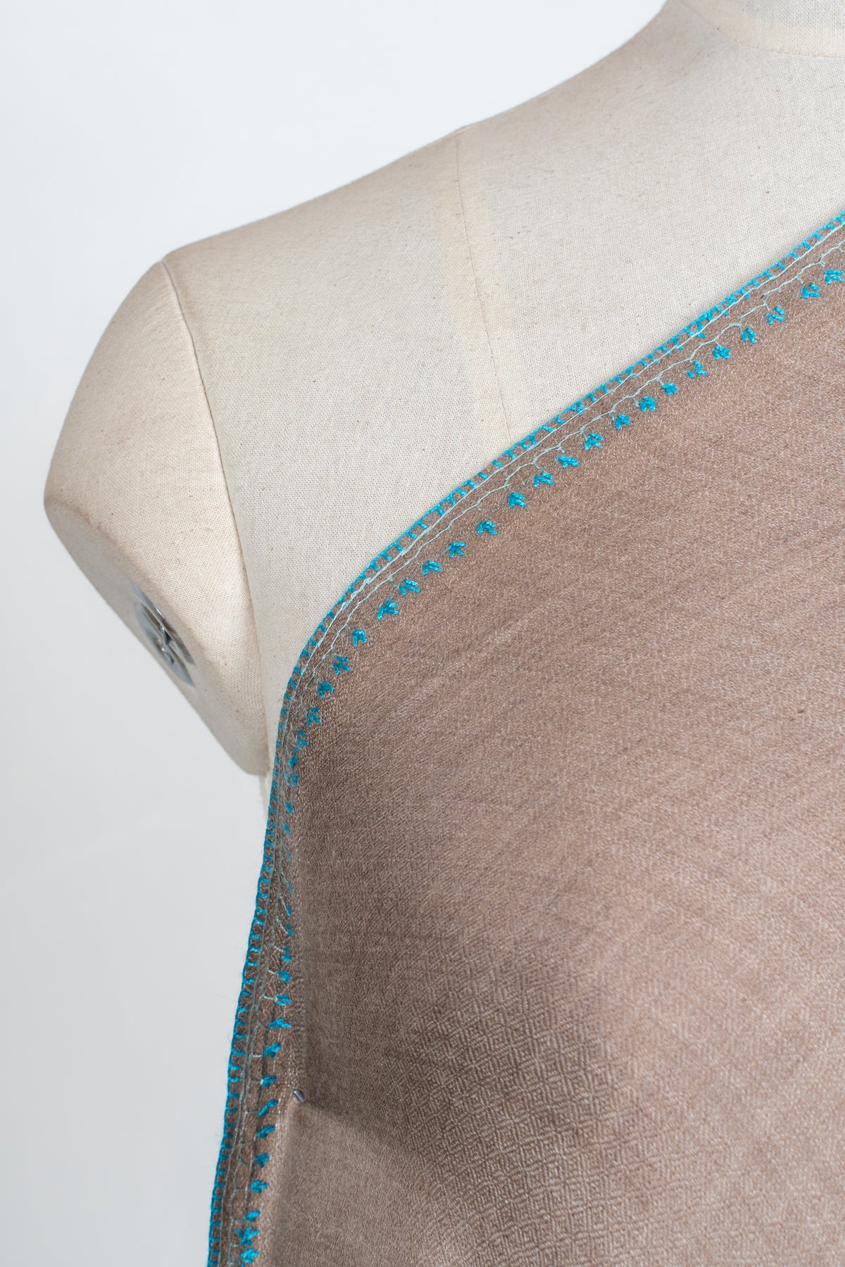 Close-up of narrow teal Sozni leaf edging along the shoulder of a walnut-brown Merino wool shawl
