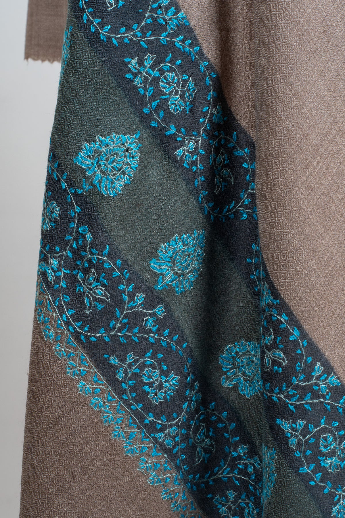 Teal Sozni floral vines and repeated small motifs across a dark end border on a walnut-brown Merino wool shawl