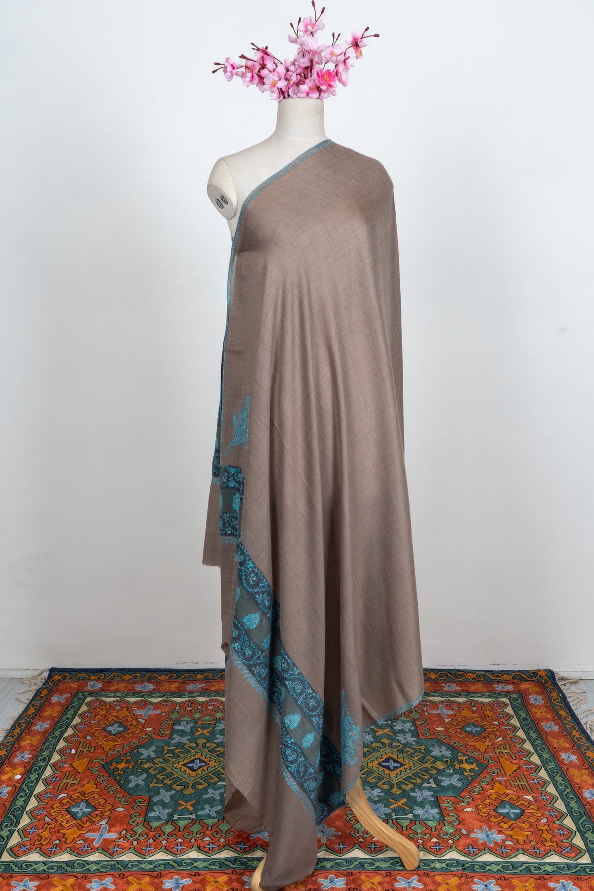 Side view of a walnut-brown Merino wool shawl on a mannequin, with teal Sozni embroidery at the lower end