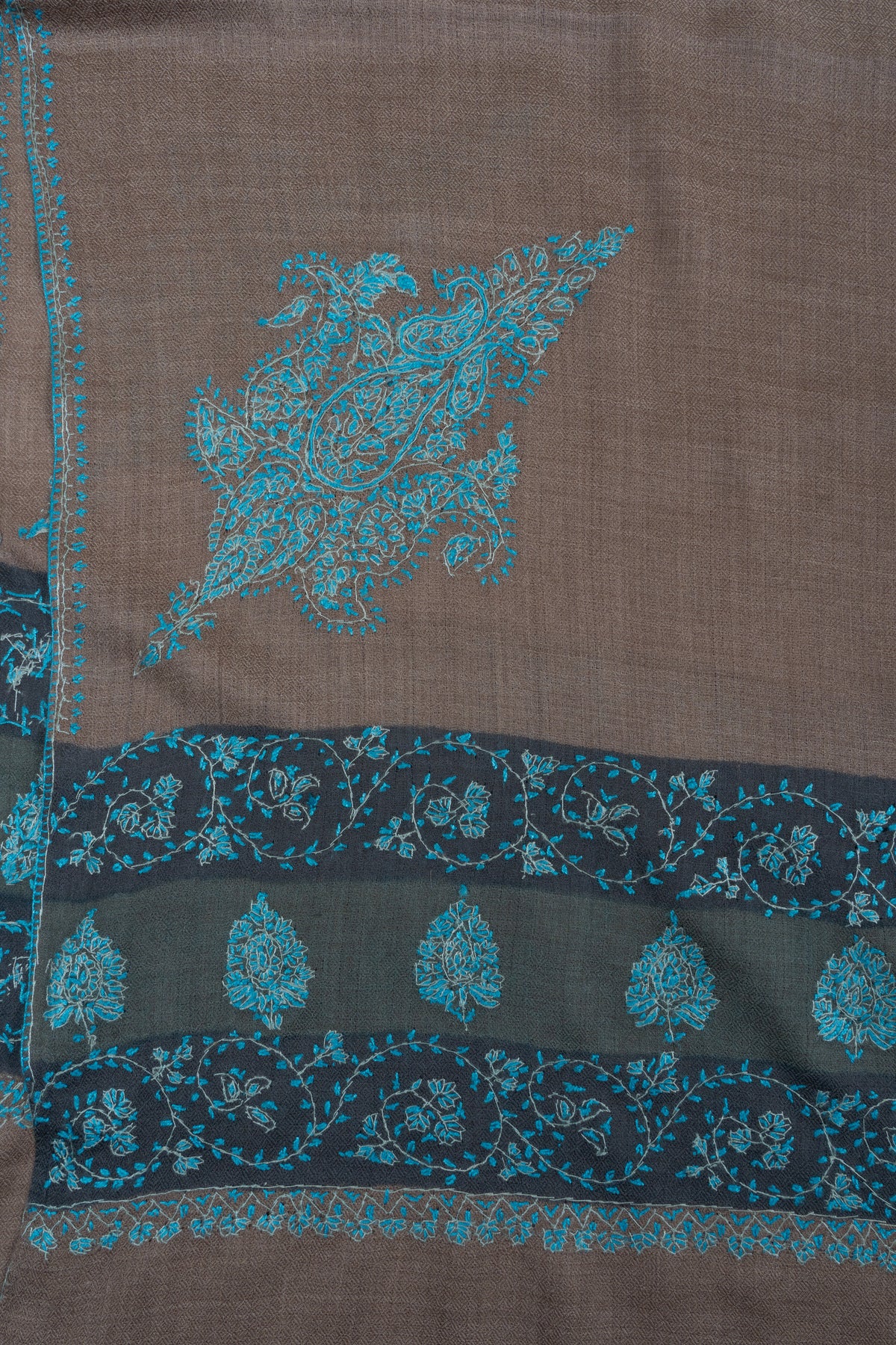 Corner of a walnut-brown Merino wool shawl, with a large teal Sozni motif above a dark floral border