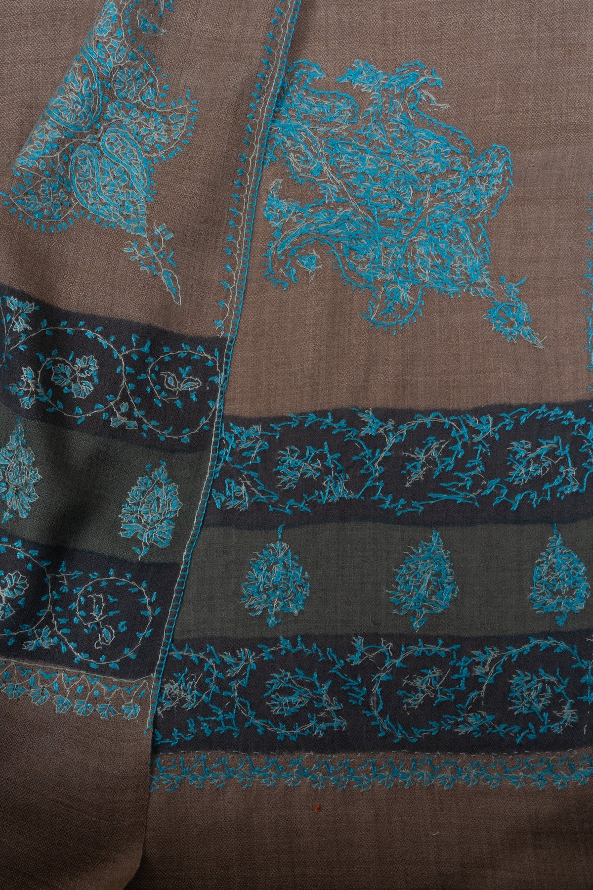 Folded walnut-brown Merino wool shawl showing matching teal Sozni corner motifs and dark embroidered borders