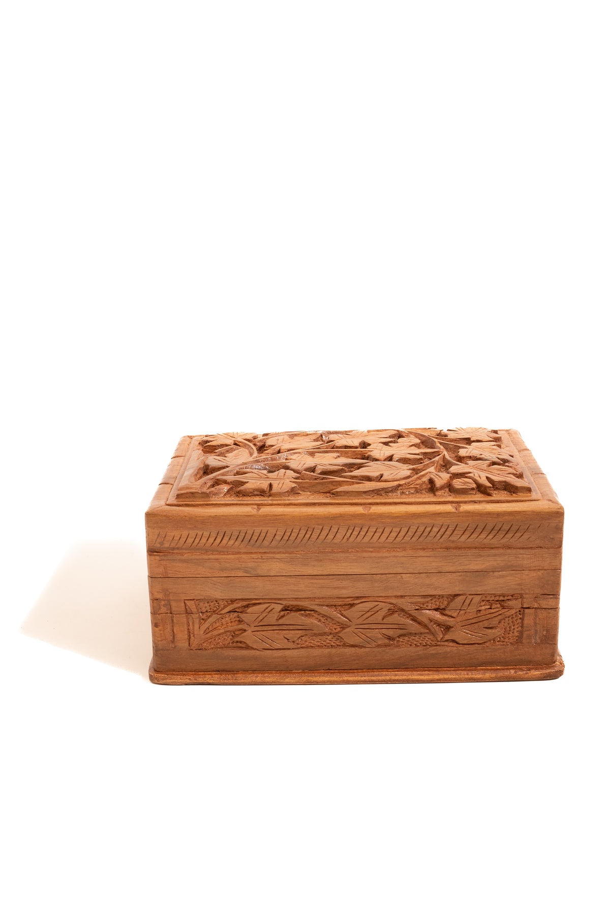 Low front view of the closed walnut box, with leaf carving on the lid and a long carved front panel