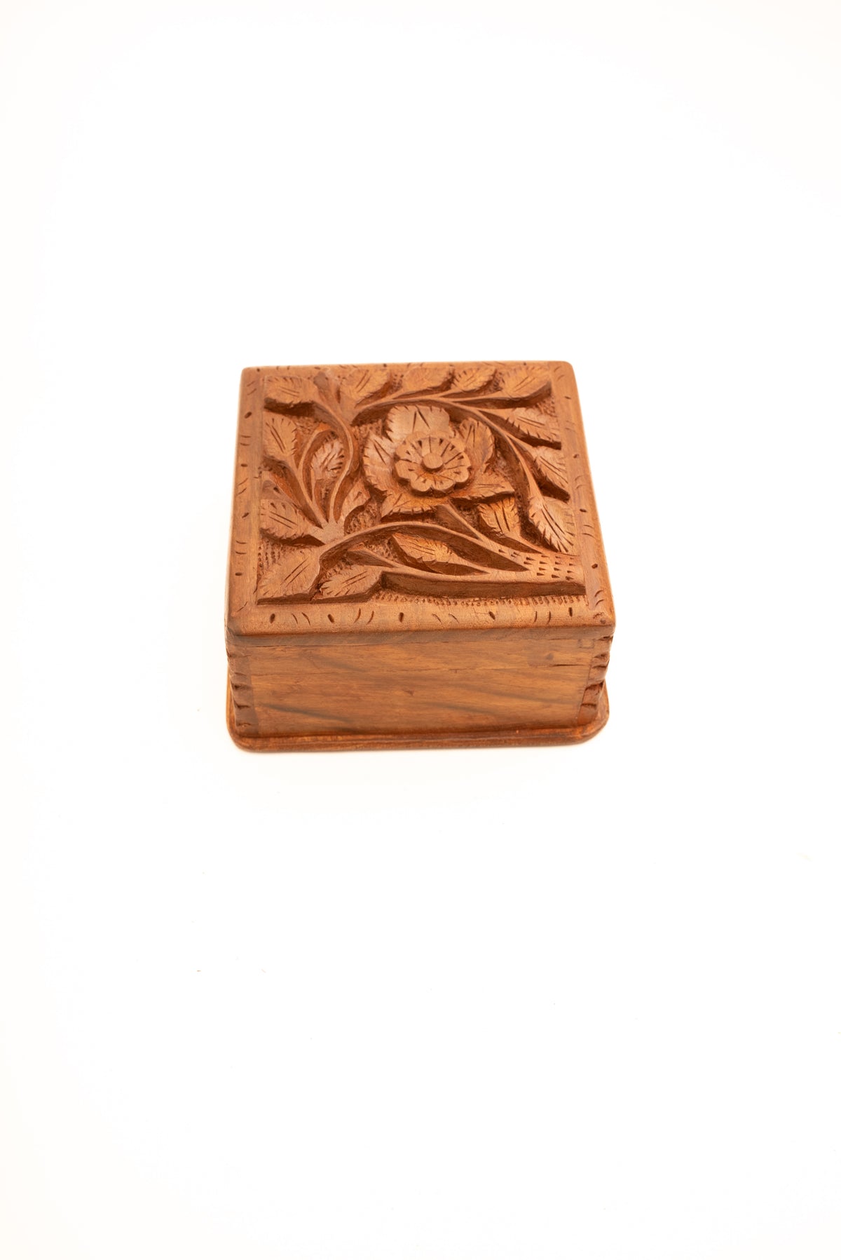 Closed square walnut wood box viewed at an angle, showing its carved floral lid and smooth front