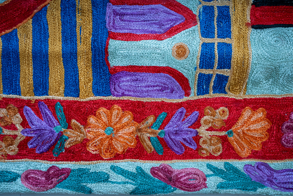 Side detail of the prayer mat showing orange and purple flowers on red beside blue and gold architectural bands