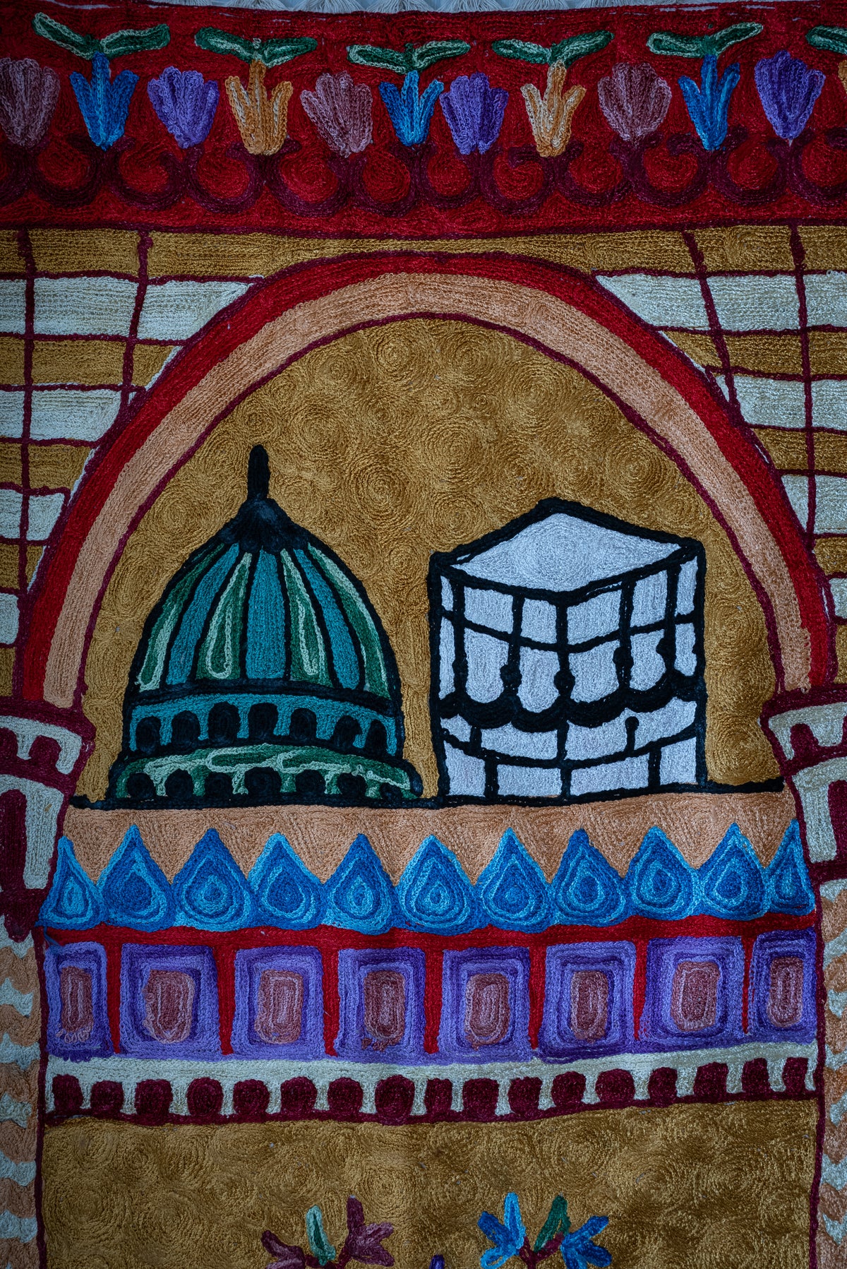 Close-up of a green dome and Kaaba motif beneath the prayer mat's golden arch