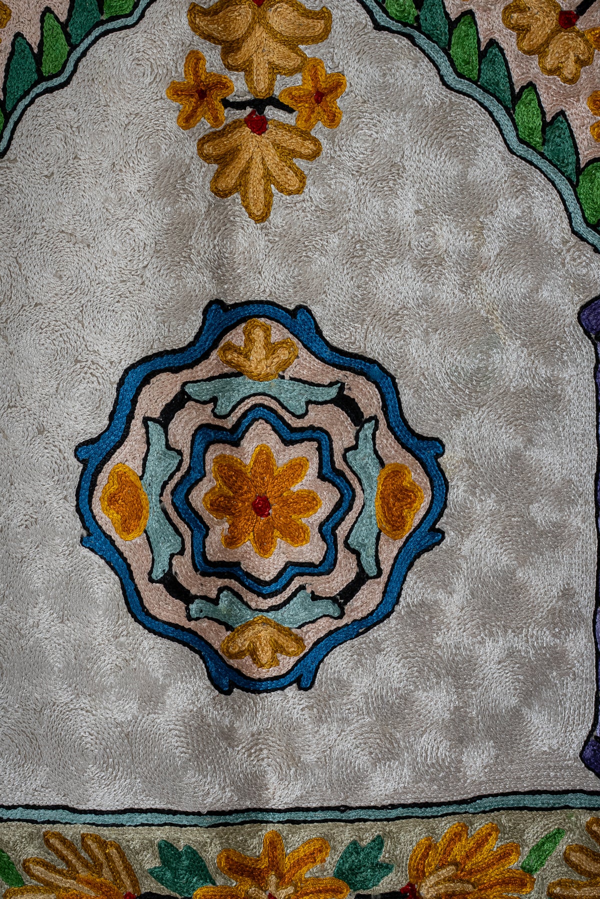 Blue, pink and gold floral medallion beneath an embroidered arch on the ivory prayer mat