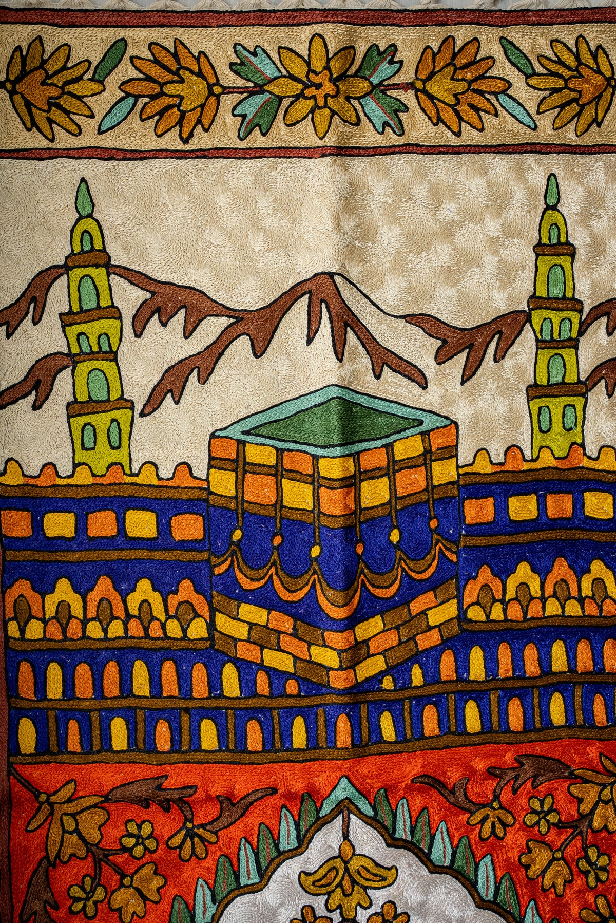 Close-up of the prayer mat's colourful Kaaba between green minarets with brown mountain silhouettes behind