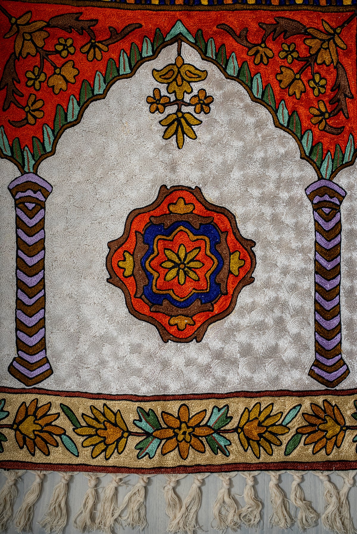 Lower end of the prayer mat with an orange and blue medallion between striped columns beneath a scalloped arch