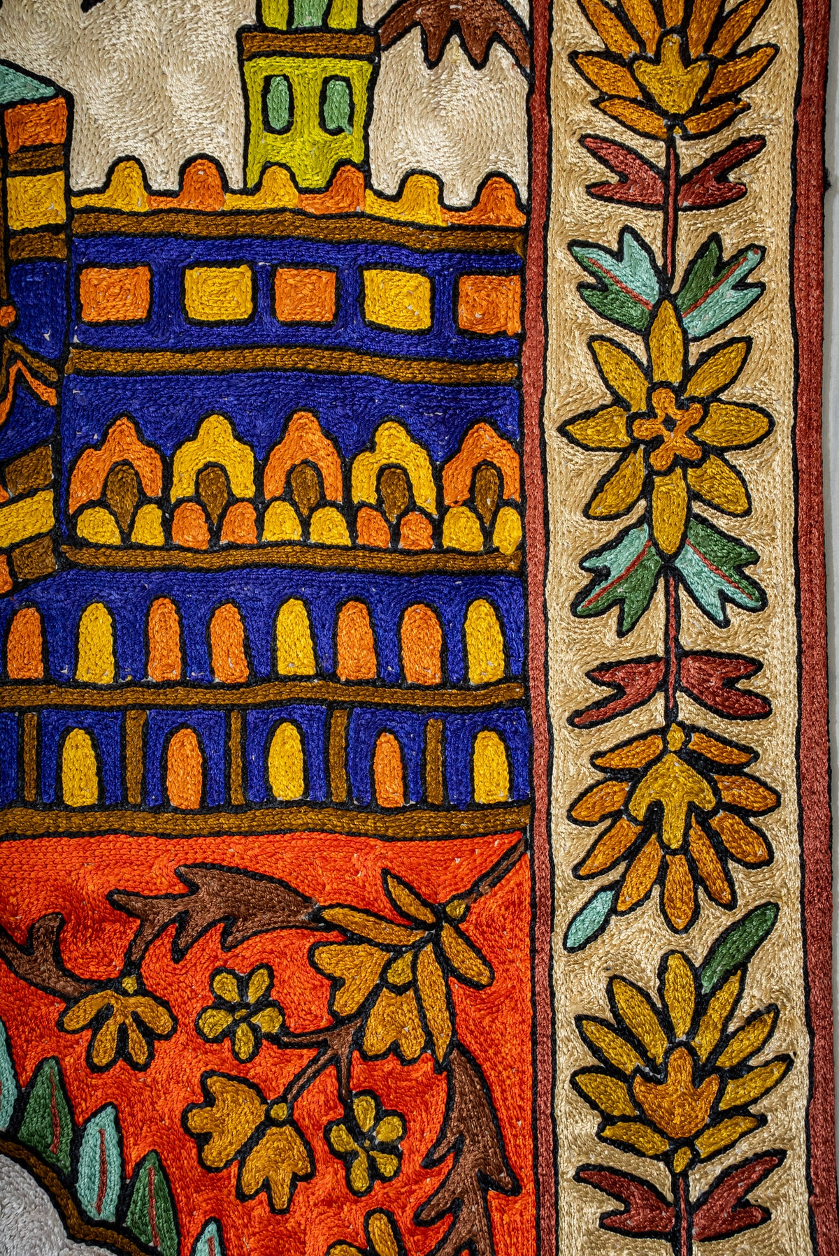 Side detail of the prayer mat with gold flowers and green leaves beside a blue and orange architectural motif