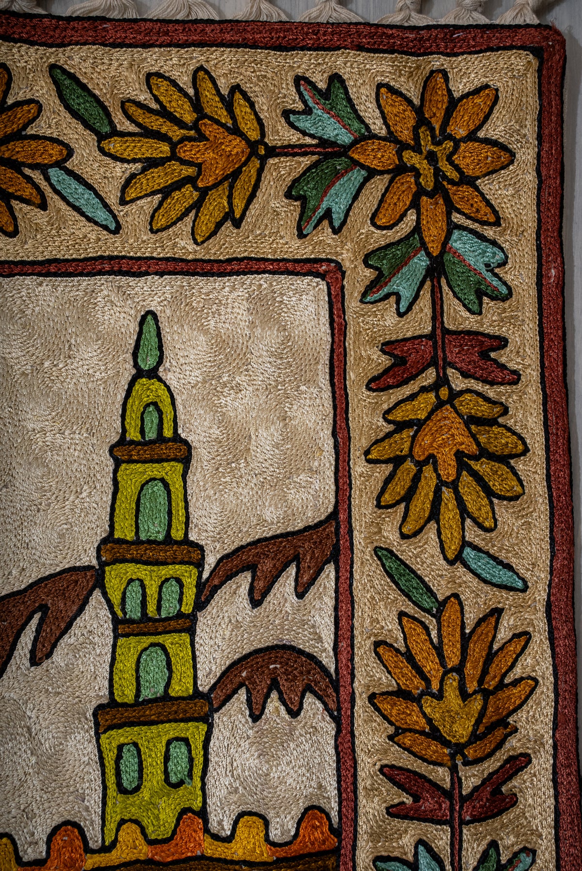 Upper corner of the prayer mat showing a green minaret, mountain outlines and gold floral border