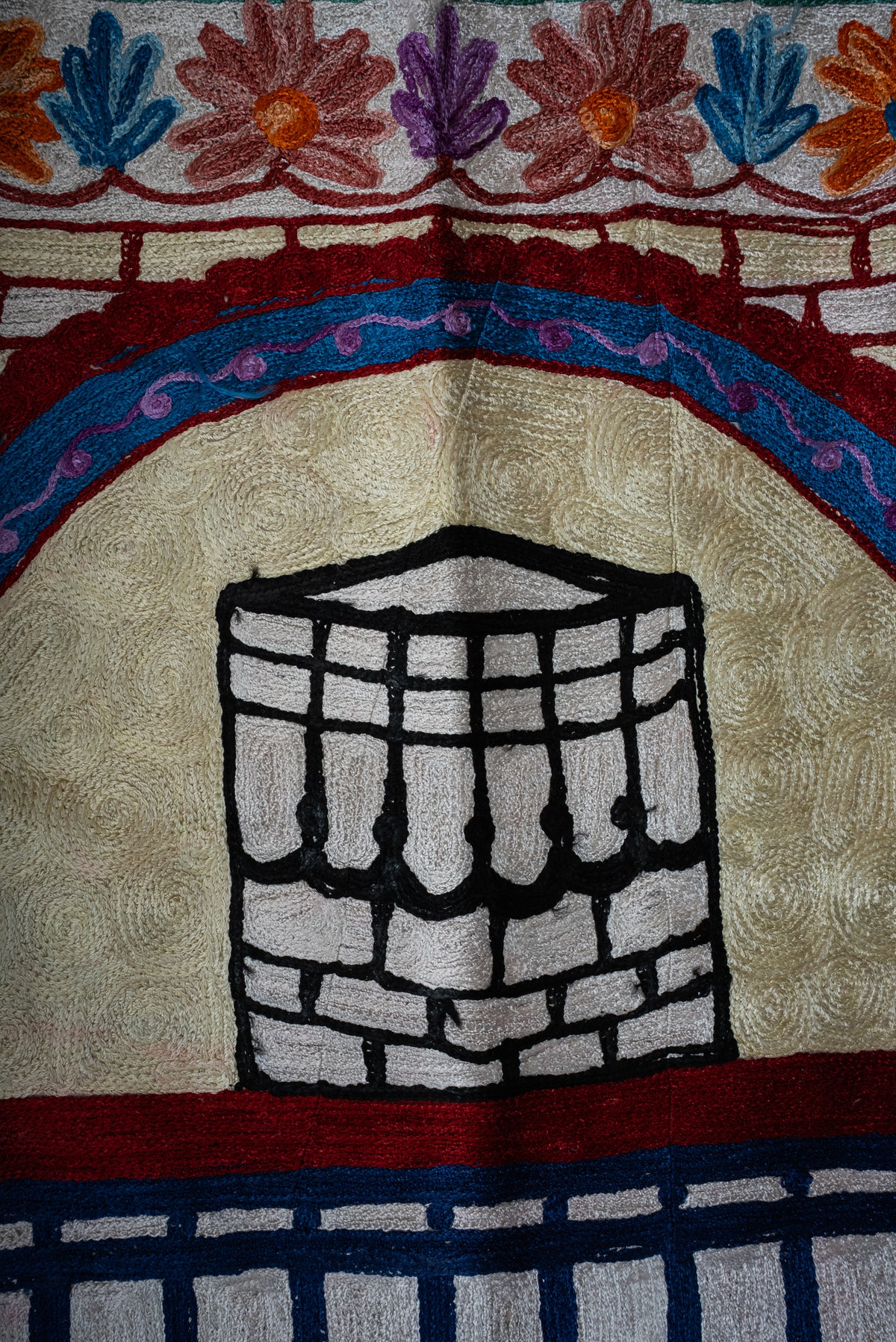 Close-up of the black-and-white Kaaba embroidered beneath a blue and burgundy arch on the prayer mat