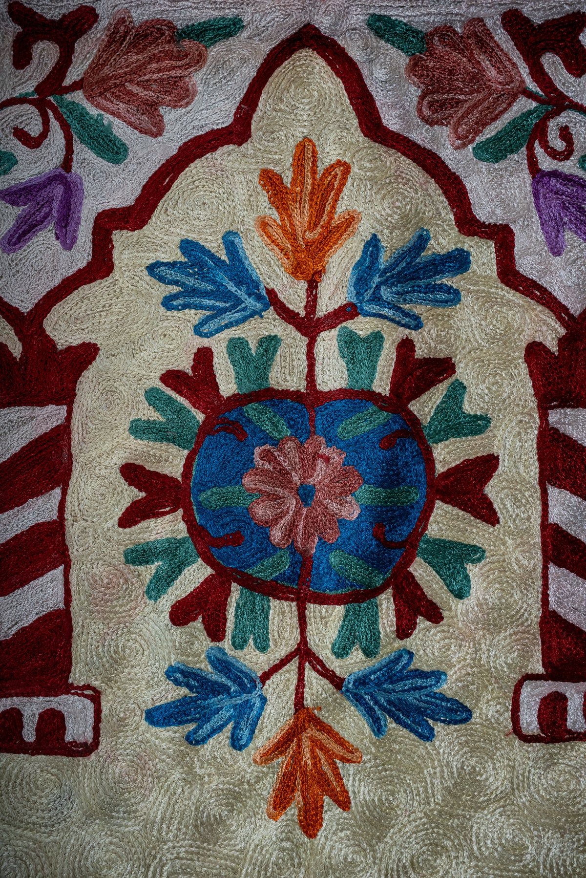 Close-up of the prayer mat's blue floral medallion between striped burgundy columns on a cream ground