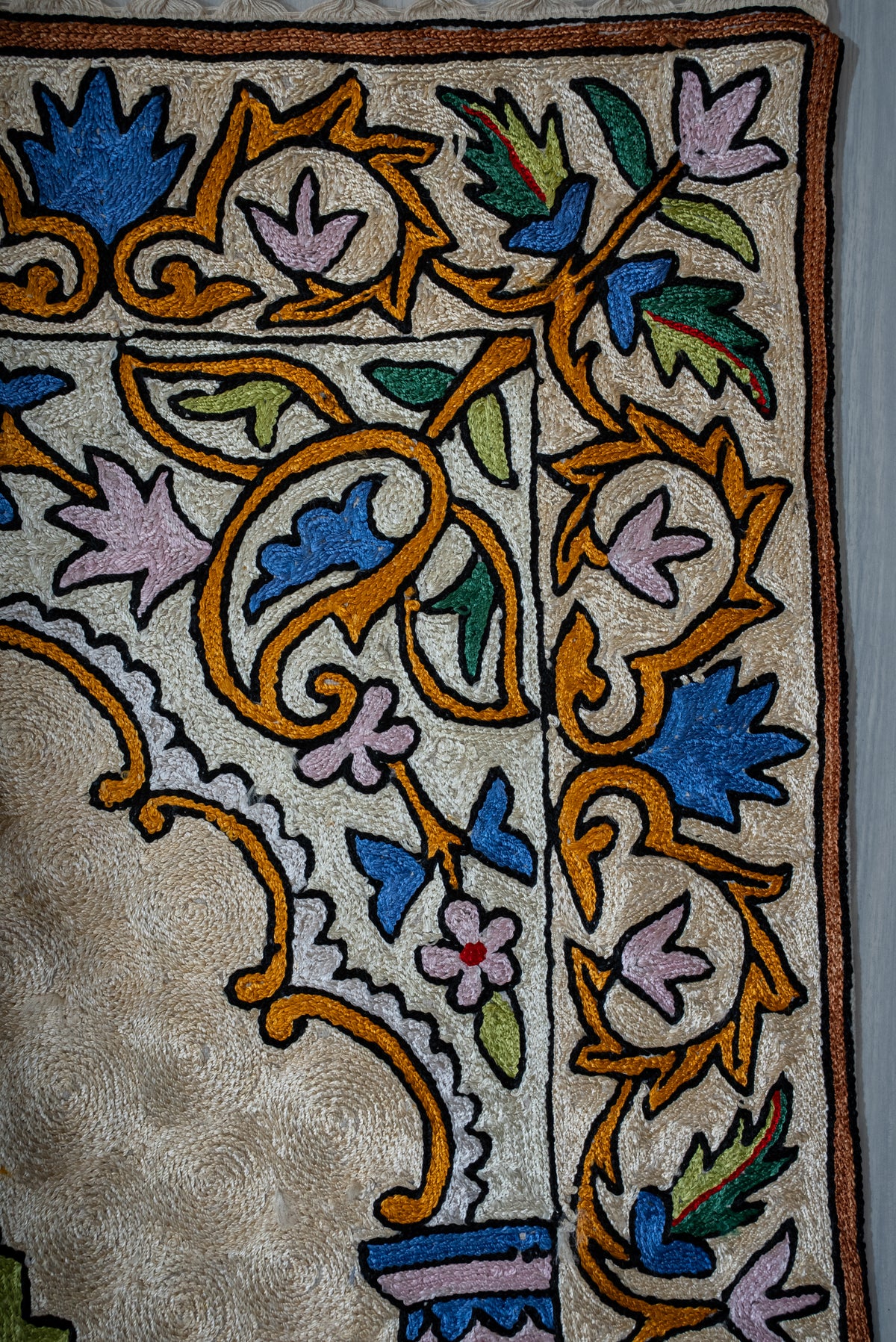 Close-up of blue and pink flowers, green leaves and golden curling stems beside the prayer mat's arch