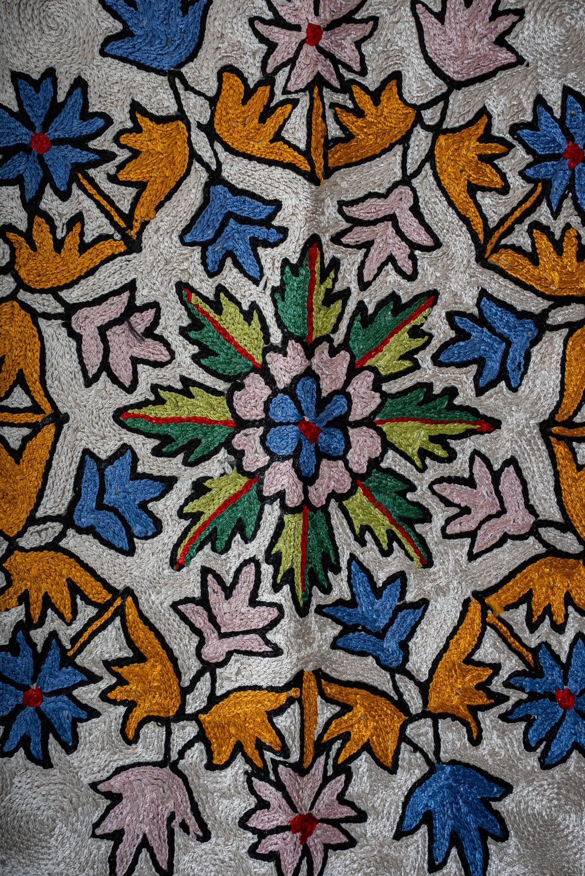 Close-up of blue, pink and gold flowers surrounding green leaves in the prayer mat's central medallion