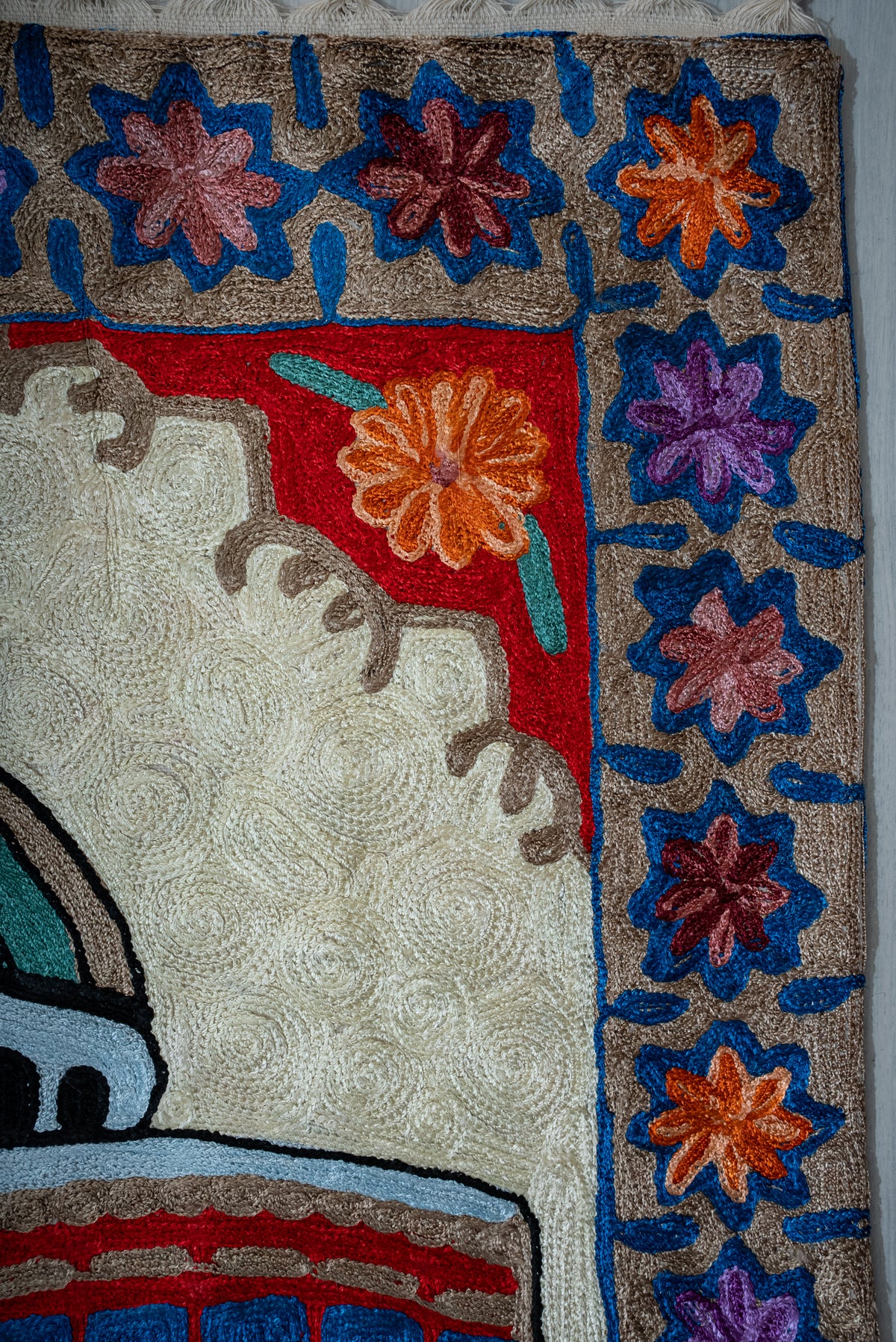 Upper corner of the prayer mat with multicoloured blue-outlined flowers beside a red arch panel