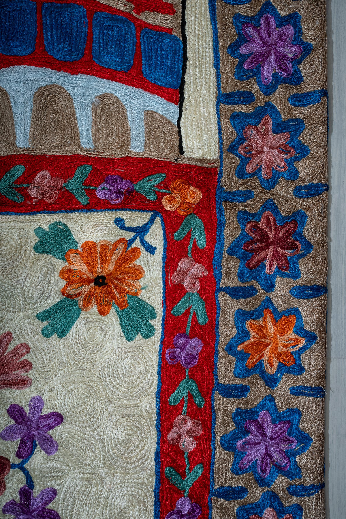 Side detail of the prayer mat with blue-outlined multicoloured flowers and a narrow red floral border