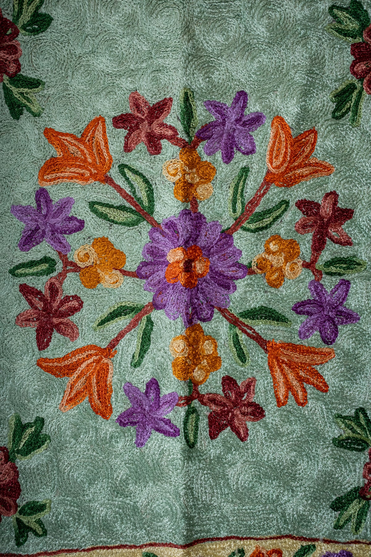 Close-up of the prayer mat's circle of purple, orange and burgundy flowers on pale green