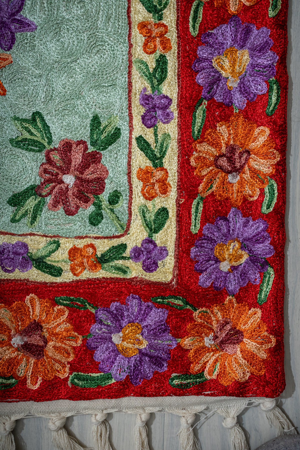 Lower corner of the prayer mat with purple and orange flowers on red, a cream inner border and tassels