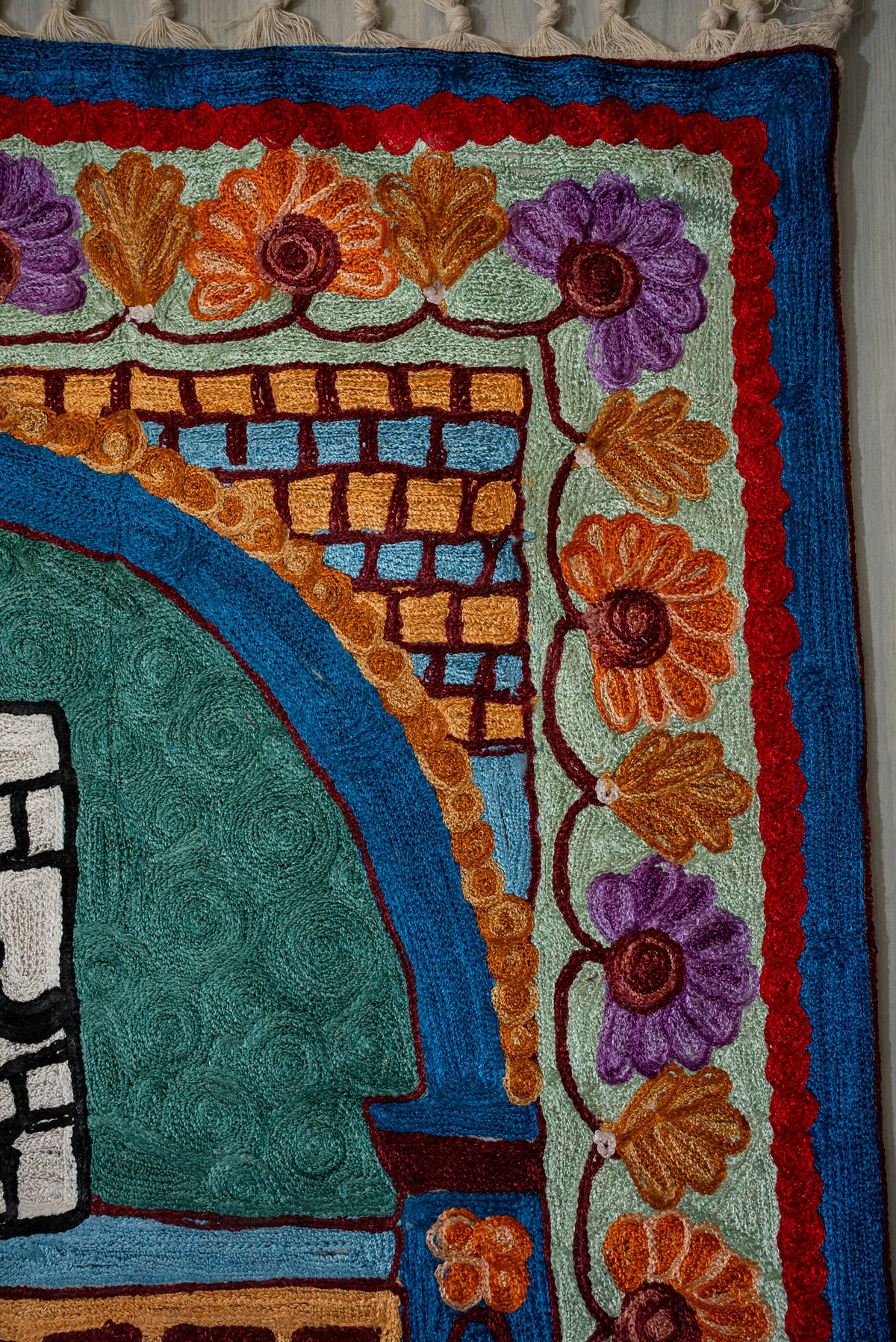 Corner detail of a prayer mat, with a blue arch, gold brick pattern and orange-purple floral border
