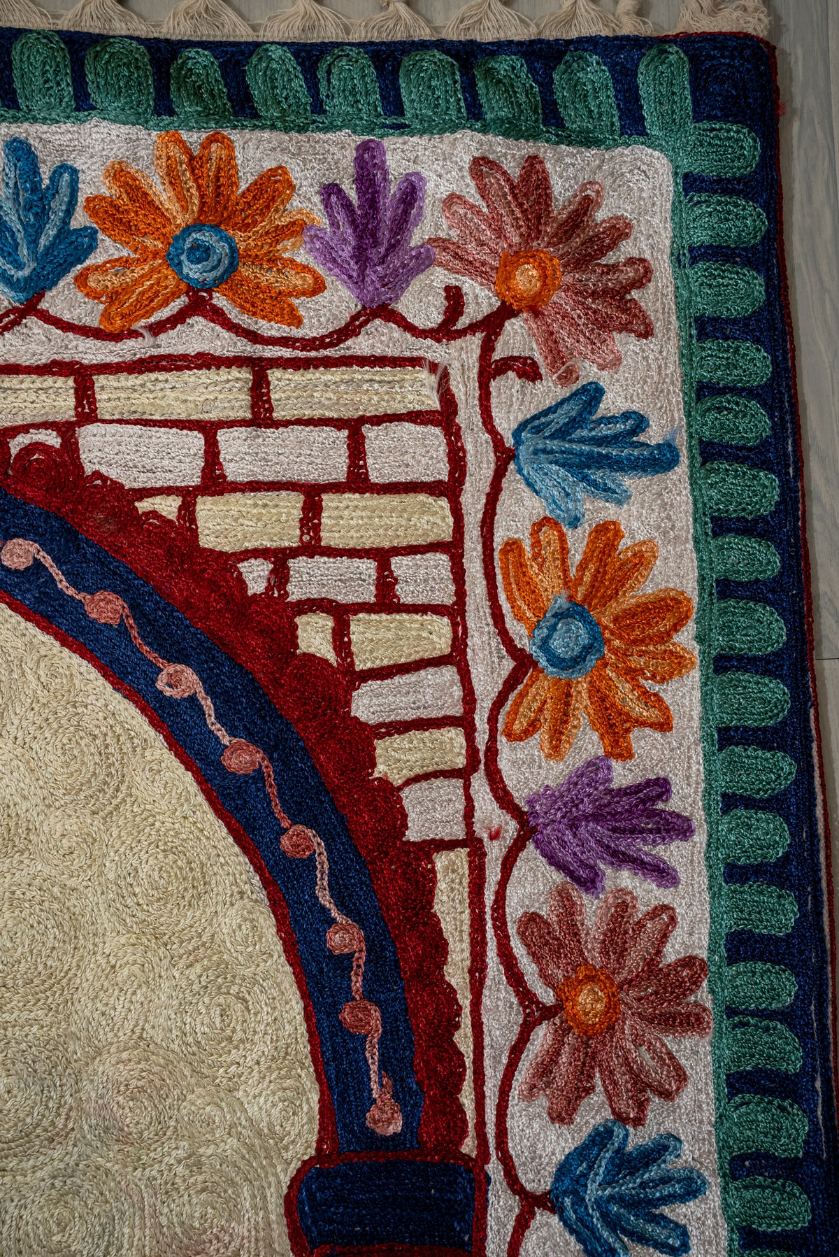 Upper corner of the prayer mat with a red brick pattern, blue arch and orange, pink and purple flowers
