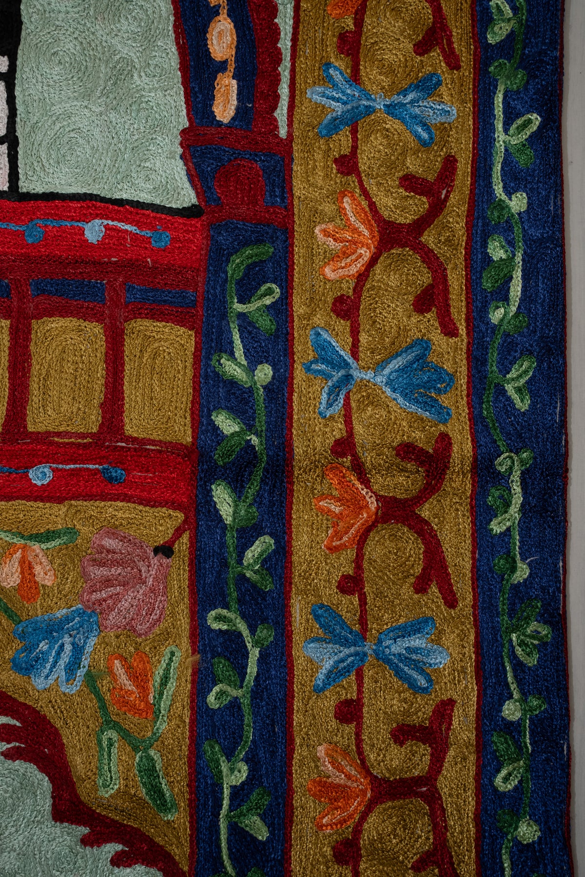 Close-up of blue and orange flowers on red curling stems along the prayer mat's gold side border