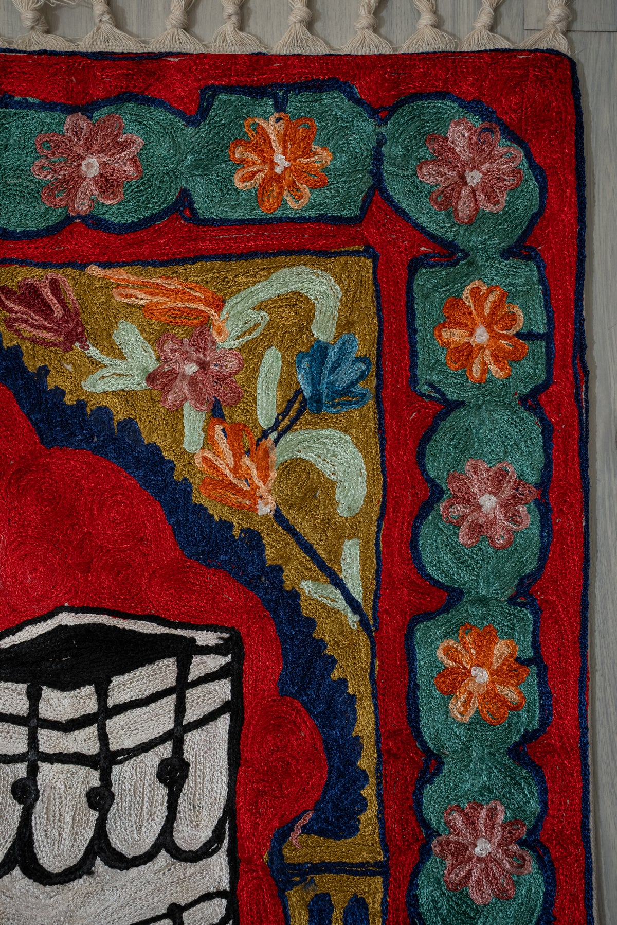 Upper corner detail of pink and orange flowers in teal panels beside the prayer mat's red arch