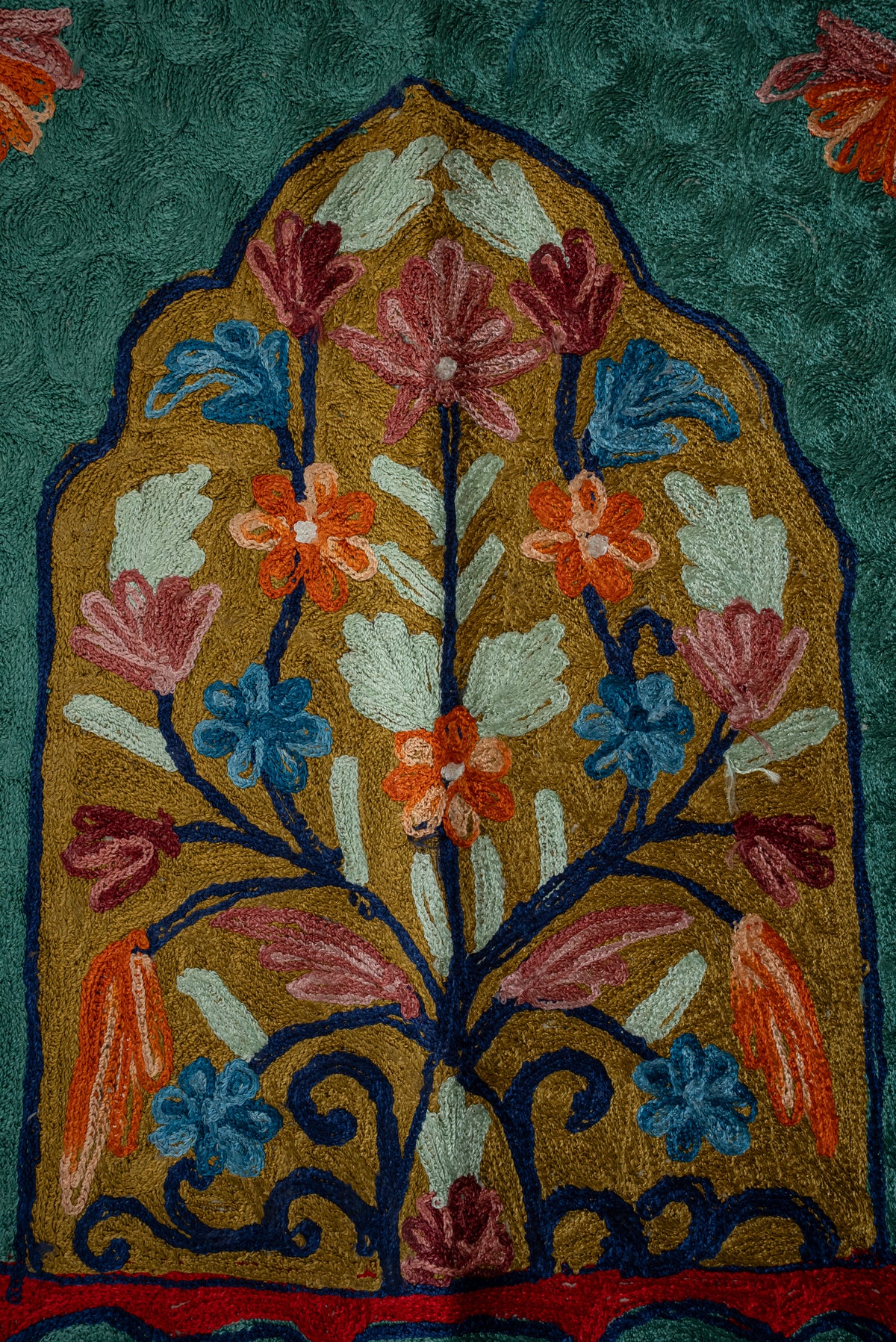 Close-up of pink, orange and blue flowers with pale leaves on dark blue stems inside a gold arched panel