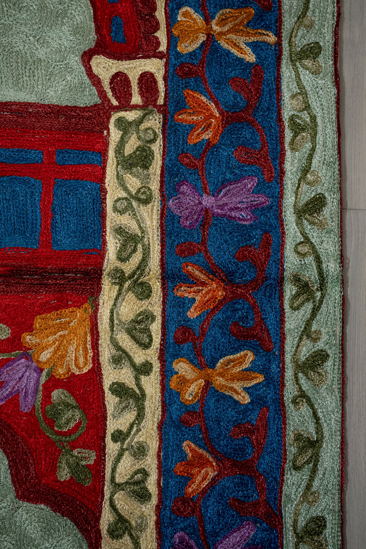 Close-up of orange and purple flowers on a blue prayer mat border, between narrow green leafy bands