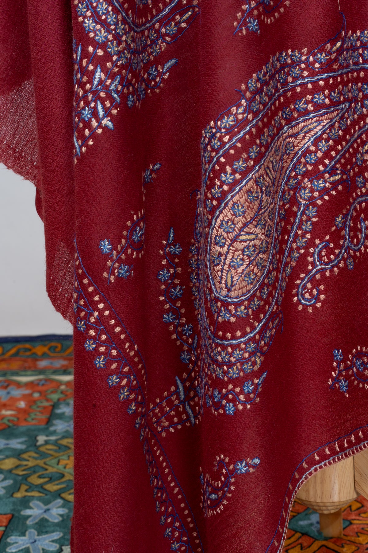 Hanging deep red shawl corner showing a large Sozni paisley filled with blue flowers and pink and gold details