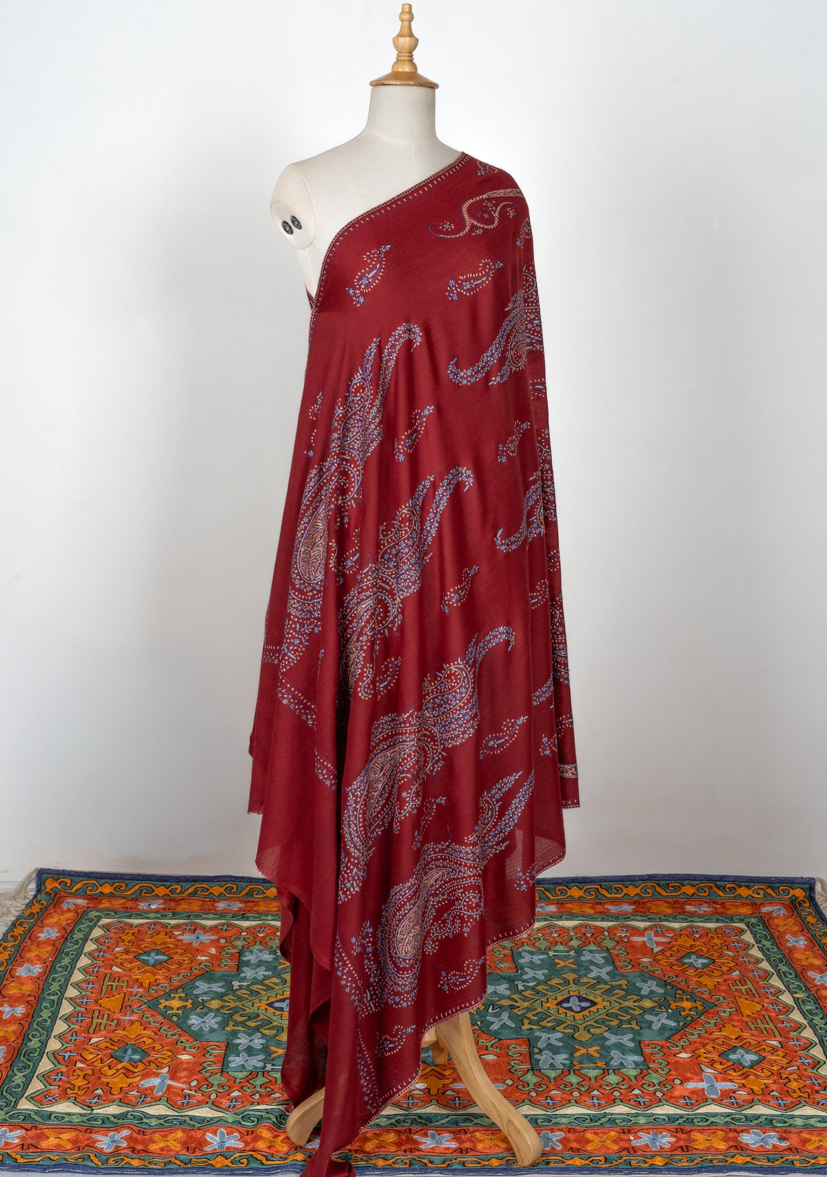 Full view of a deep red shawl on a mannequin, with large multicoloured Sozni paisley medallions and smaller scattered motifs
