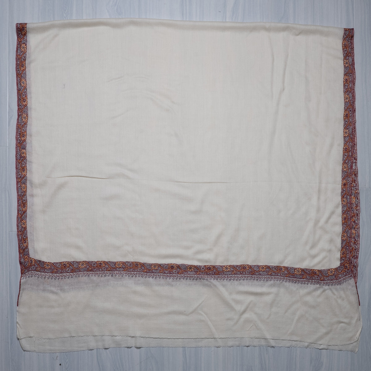 Ivory Merino wool shawl spread flat with a plain field and burgundy, orange and pale embroidered borders