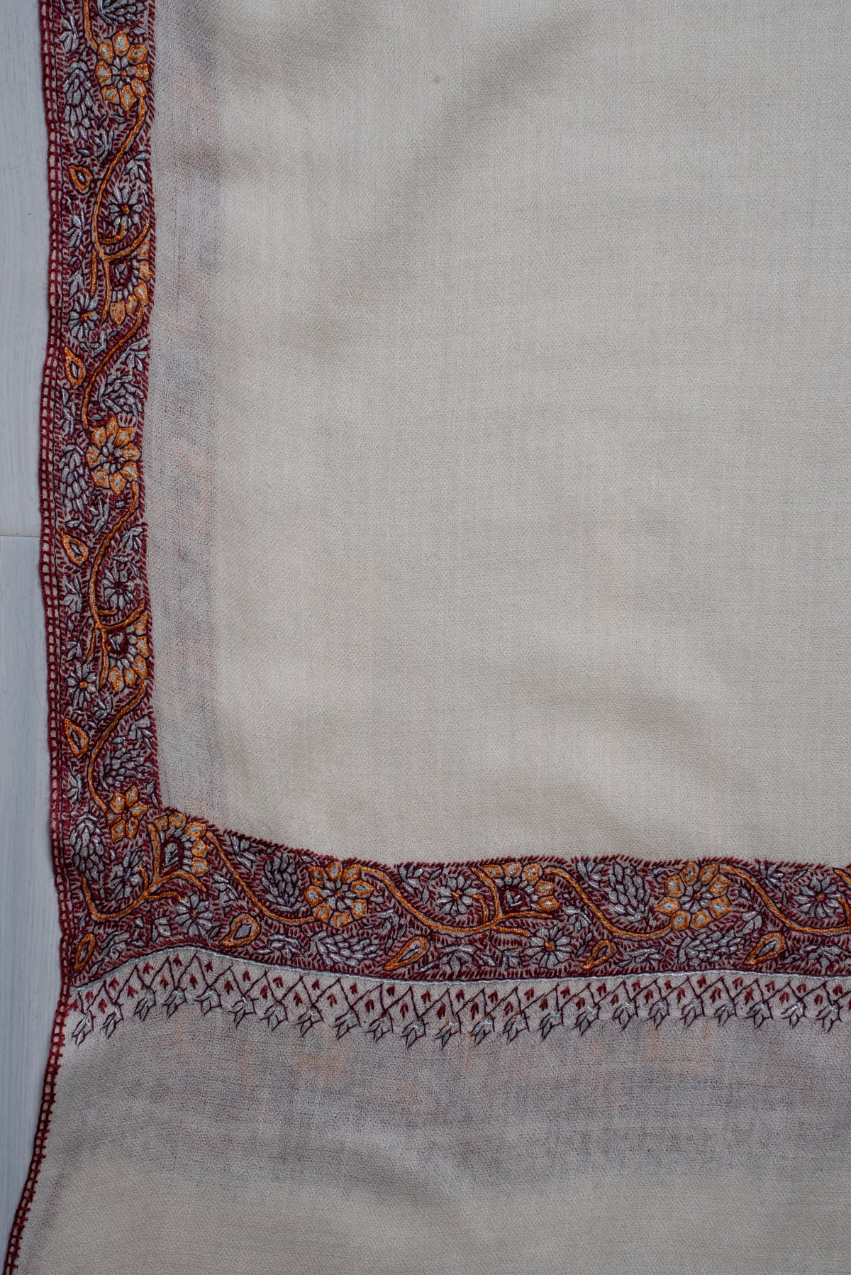 Corner detail of the ivory shawl with a narrow floral border and rows of small hanging leaf motifs