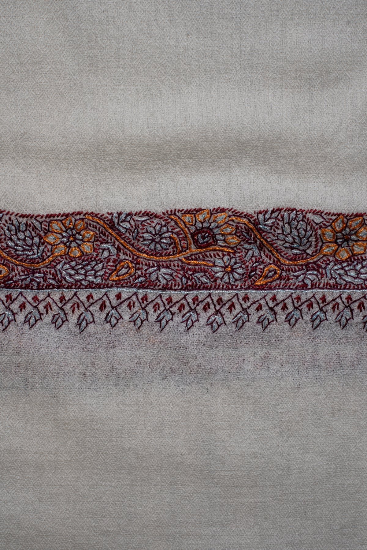 Close-up of the ivory shawl's burgundy and orange floral border with delicate dangling motifs