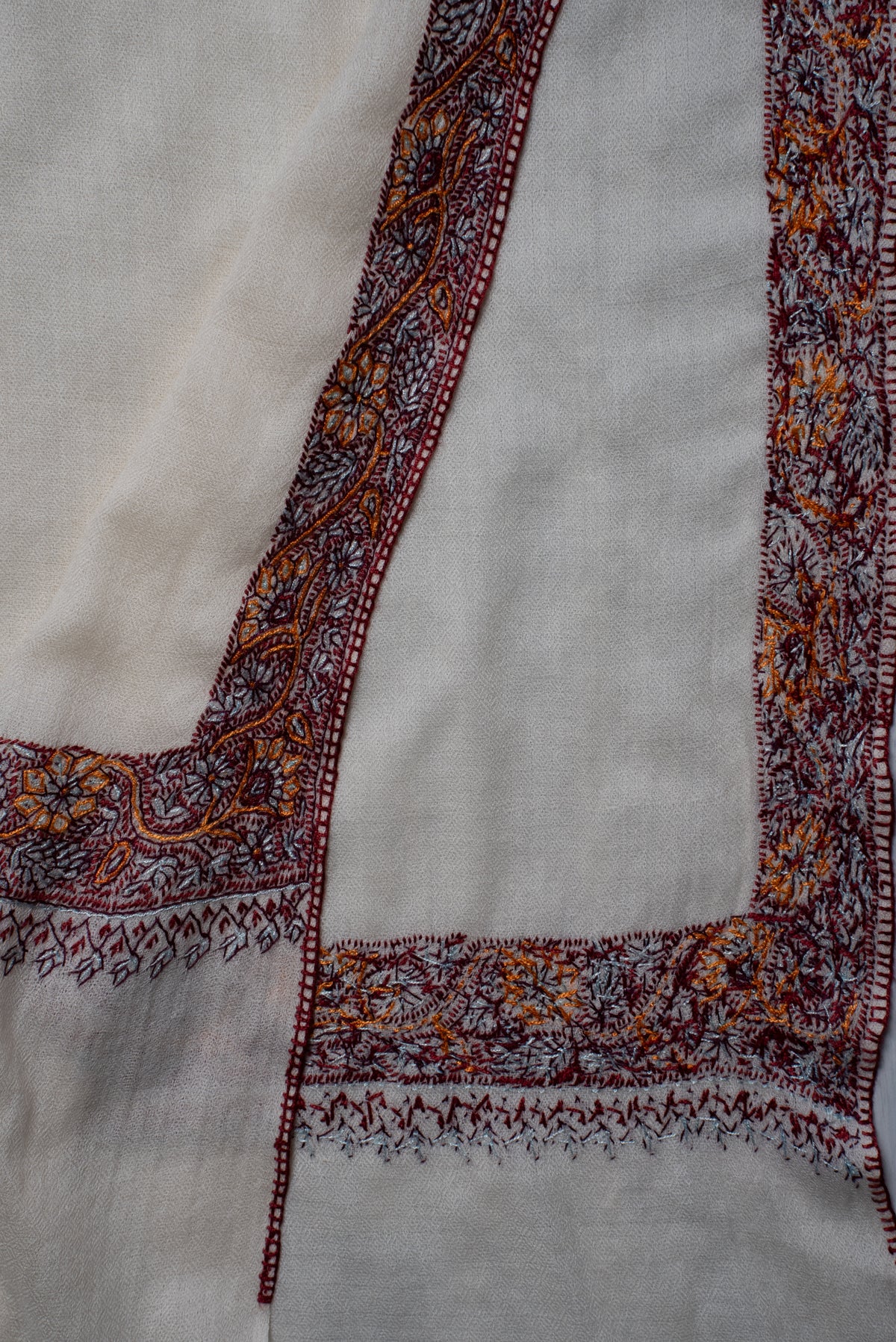 Folded ends of the ivory shawl showing its burgundy and orange embroidery on both sides