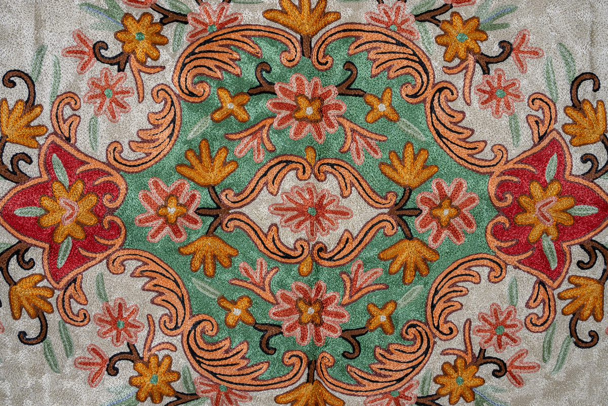 Central green medallion of an Aari chain-stitch rug with symmetrical coral and gold flowers and peach scrolling foliage