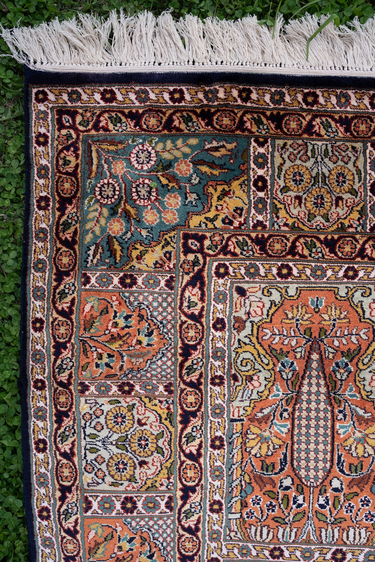 Corner of a silk carpet with framed tree and floral panels, layered dark borders and cream fringe