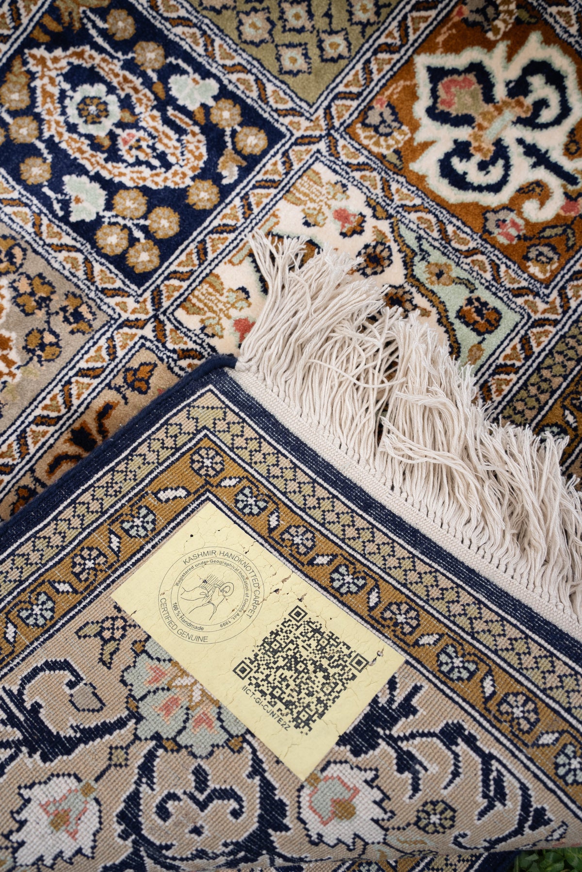Folded carpet corner showing the patterned underside, white fringe and a pale QR-coded label