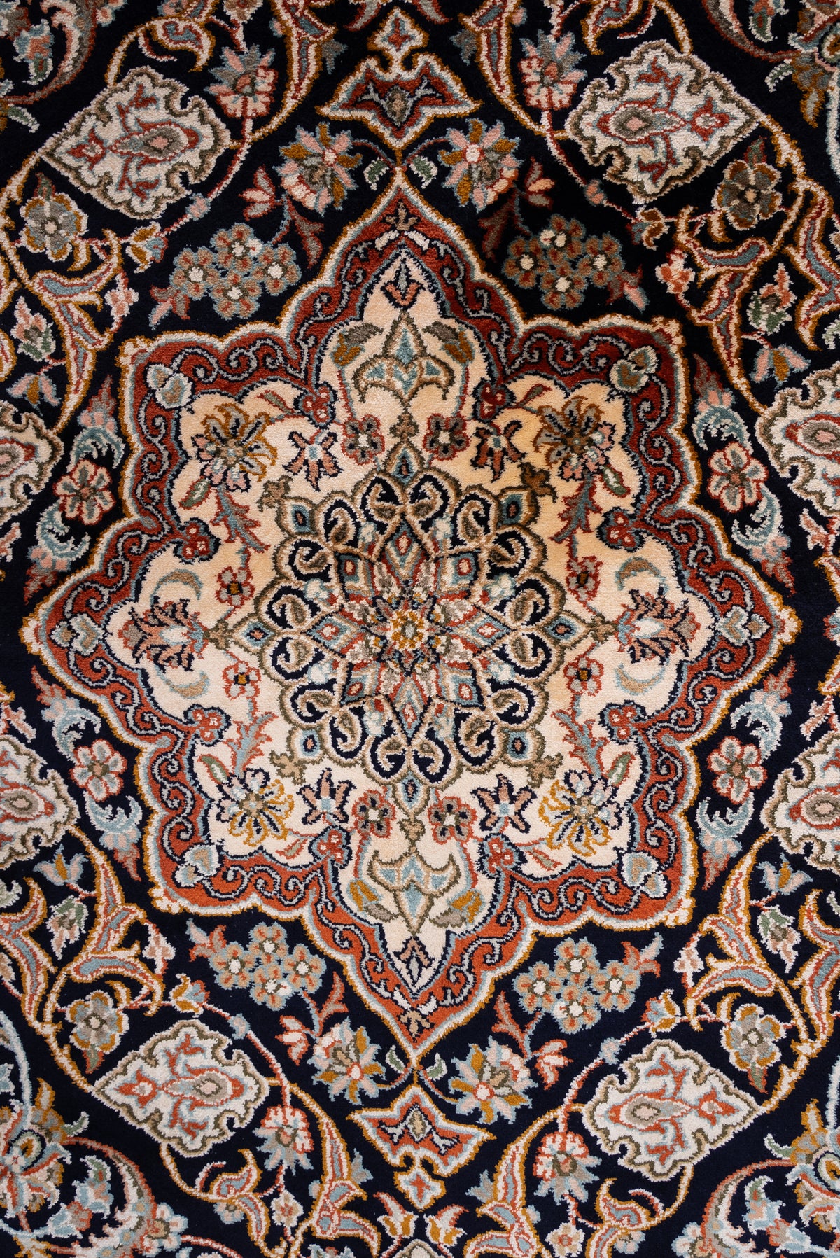 Close-up of the cream and rust floral medallion on the dark field of a mulberry silk carpet
