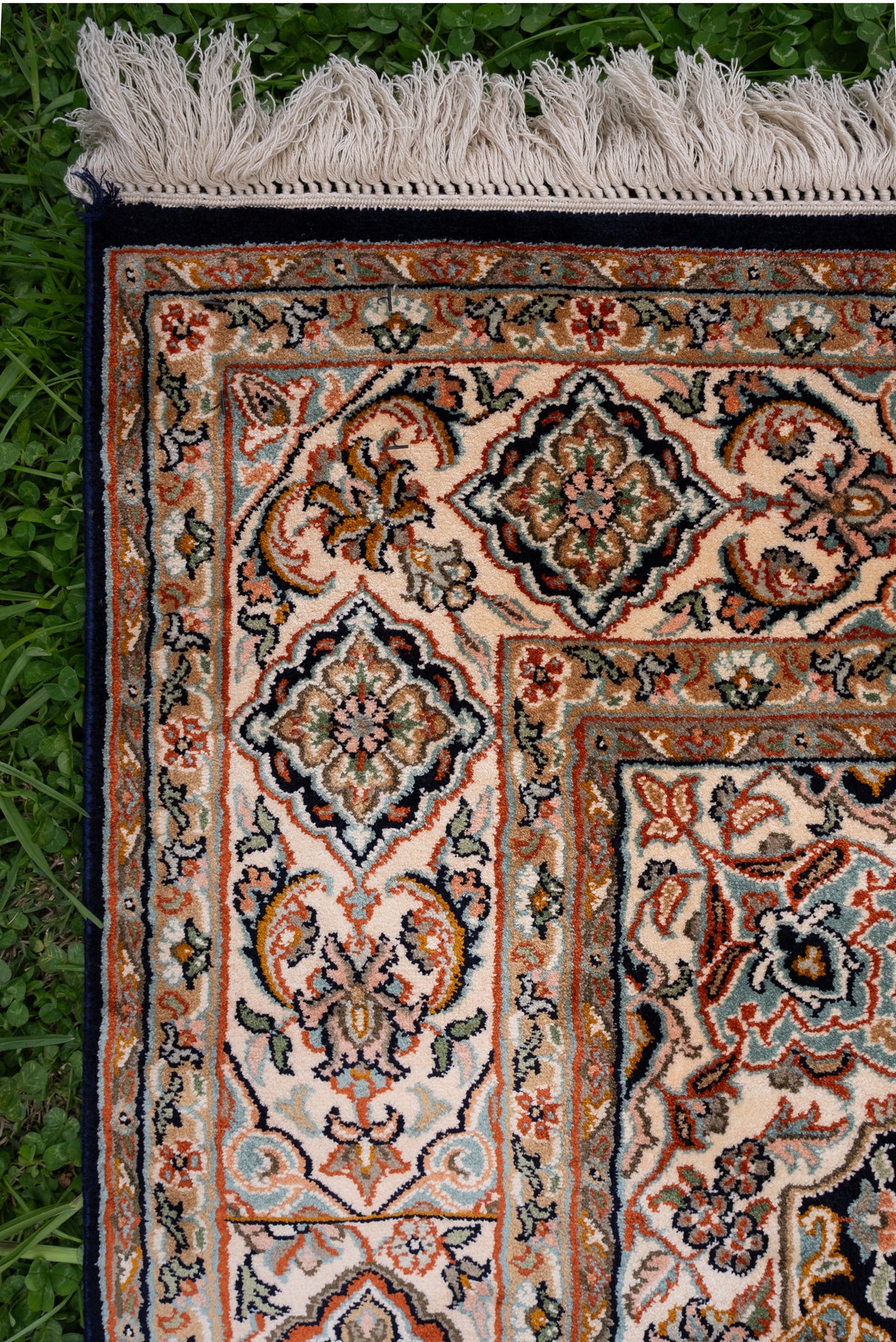 Upper corner of a mulberry silk carpet with cream floral borders, rust outlines, dark edging and ivory fringe