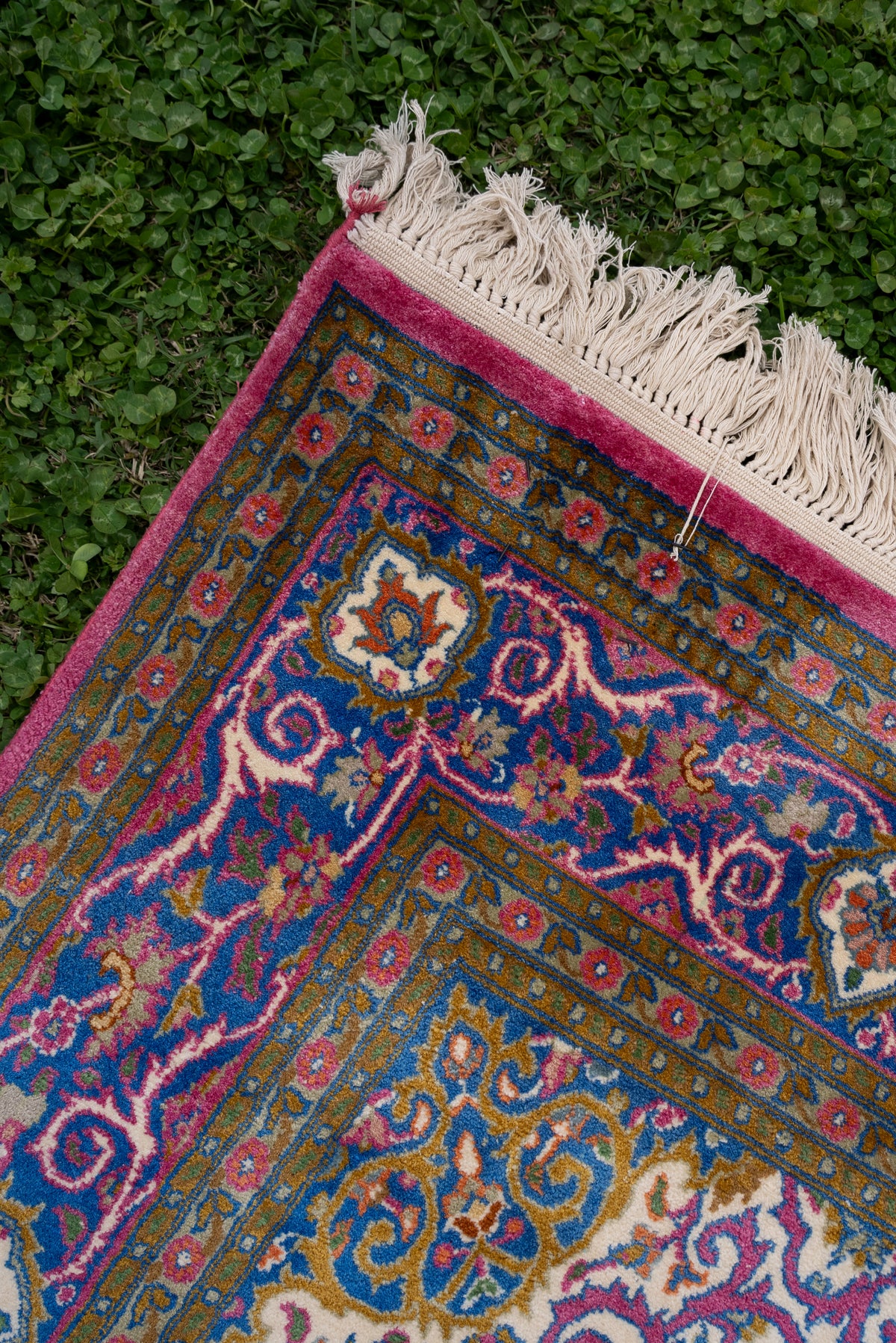 Carpet corner on grass showing blue floral borders, a rose edge and ivory fringe