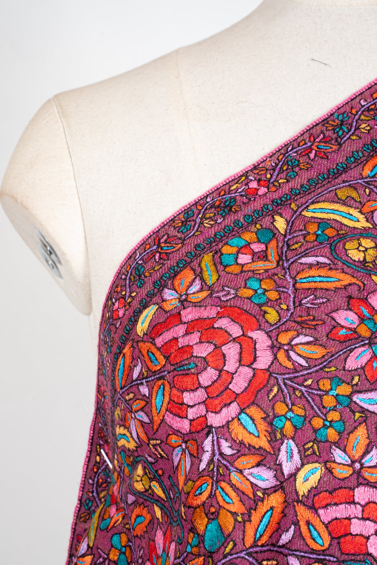Close-up of pink and red flowers, orange leaves and small turquoise blossoms embroidered on plum Pashmina