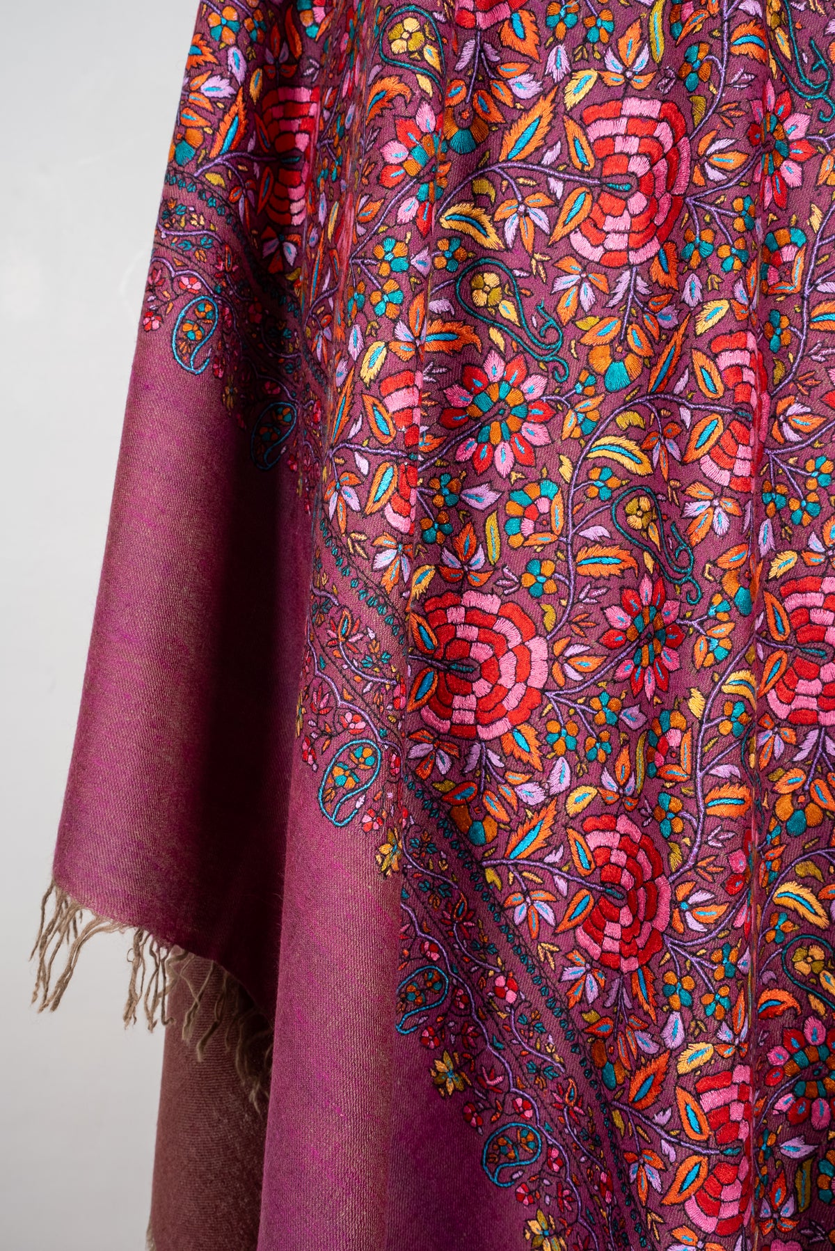 Plum Pashmina shawl hanging in folds, with dense colourful floral embroidery beside a plain fringed end